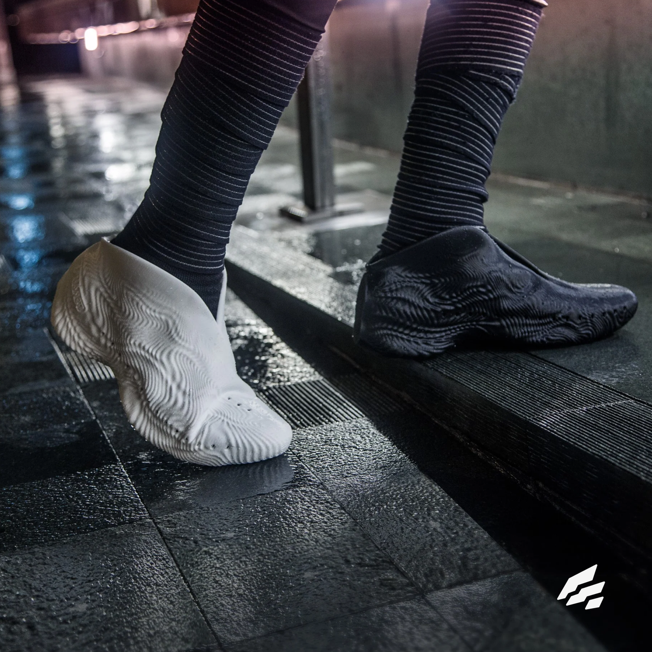 Feet in mismatched white and black 3D-printed shoes on wet stone, with the Fused mark