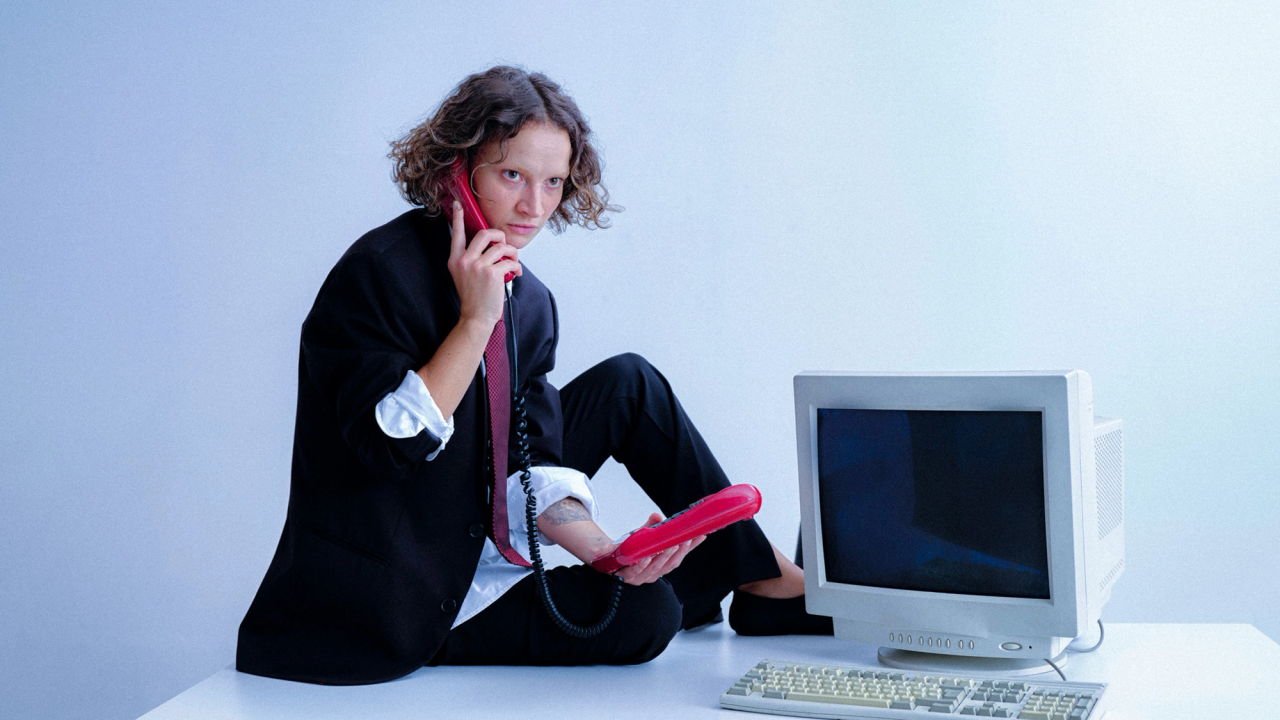 A woman in a black suit on an office desk, holding a red phone