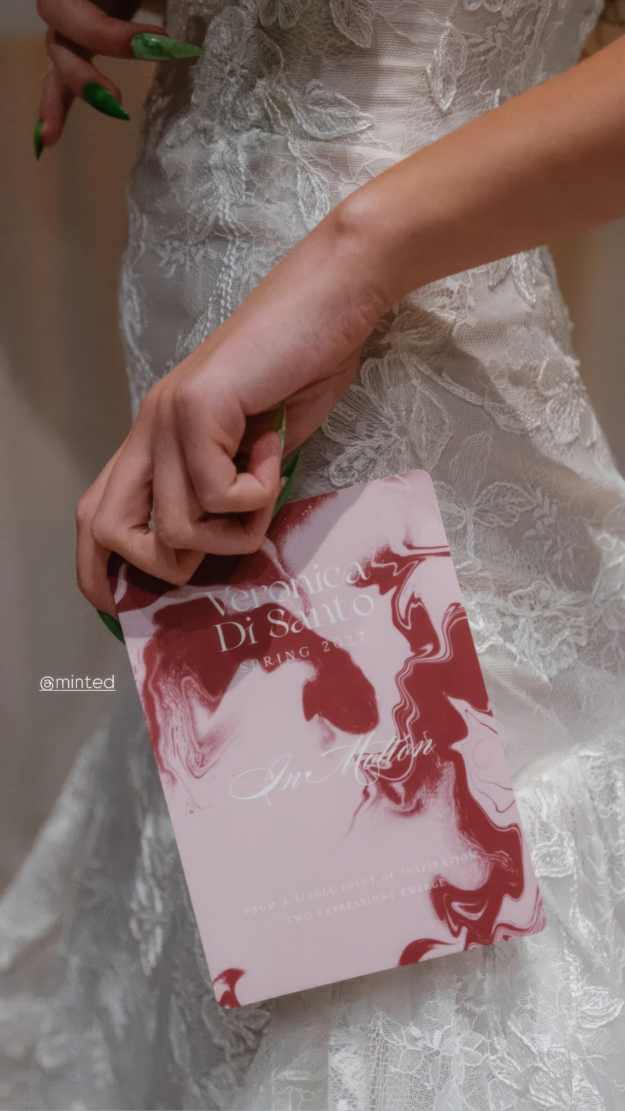 A marbled pink Veronica Di Santo card held against a white lace gown