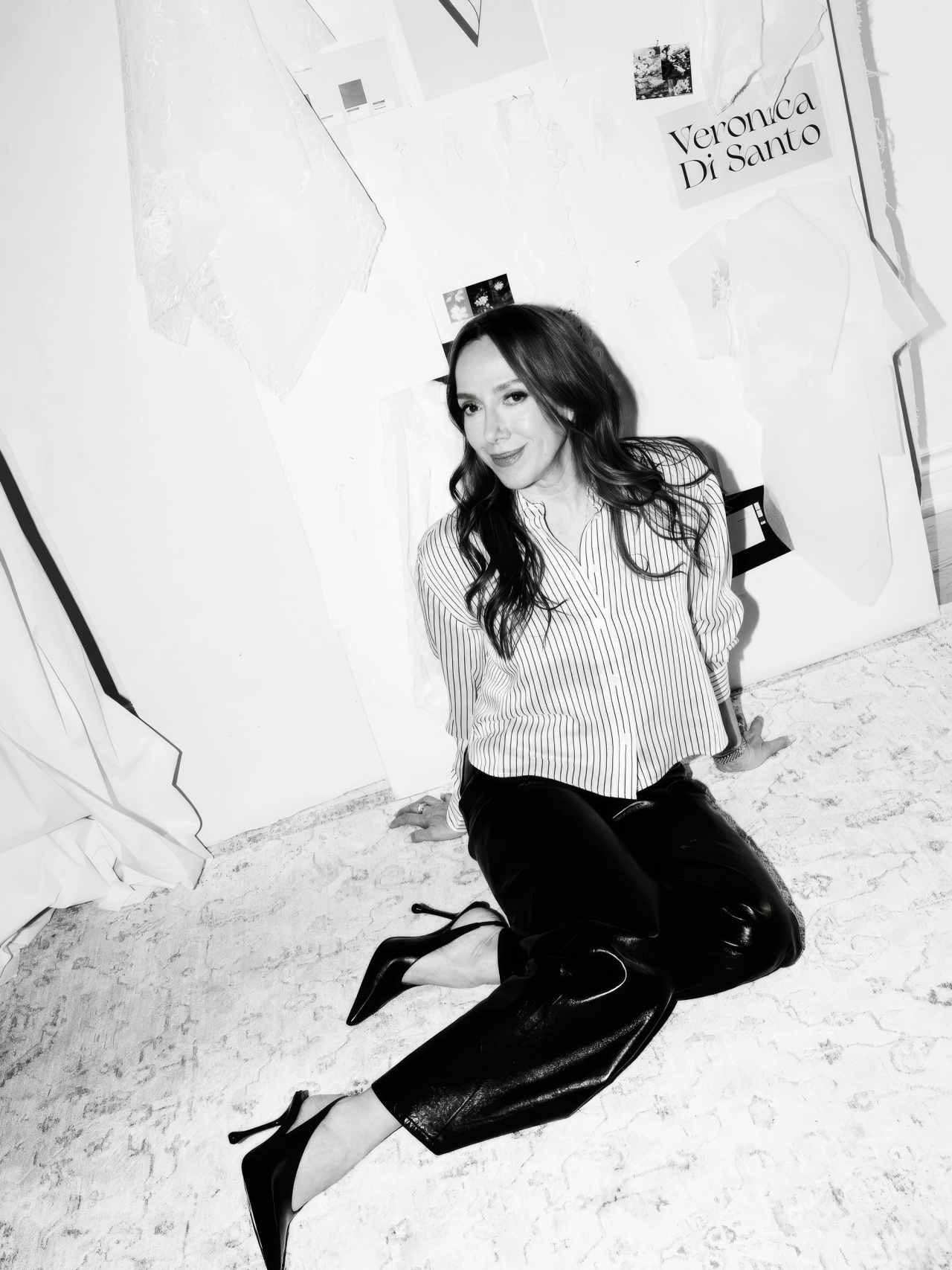 A woman in a striped shirt on the floor below a Veronica Di Santo sign