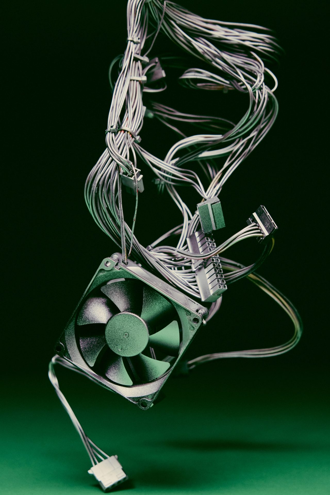 A computer fan dangling from a tangle of gray wires against dark green