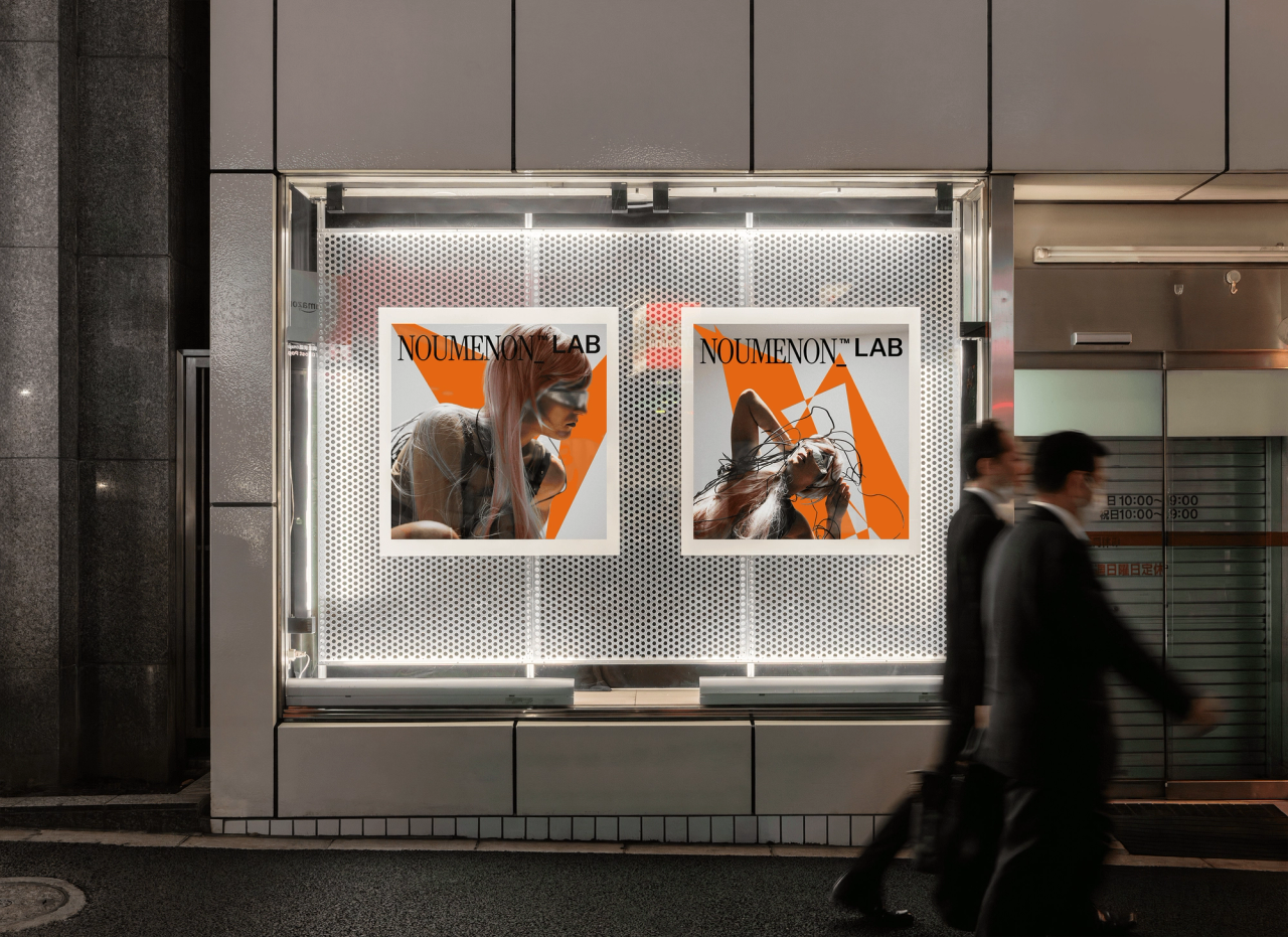 Two NOUMENON LAB posters in a lit display window as two men in suits walk past