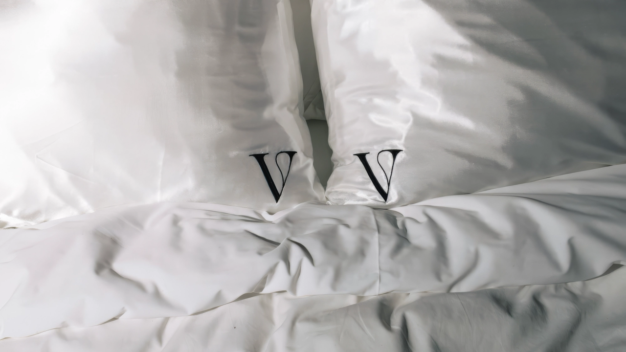 Two white pillows bearing the V monogram on an unmade bed
