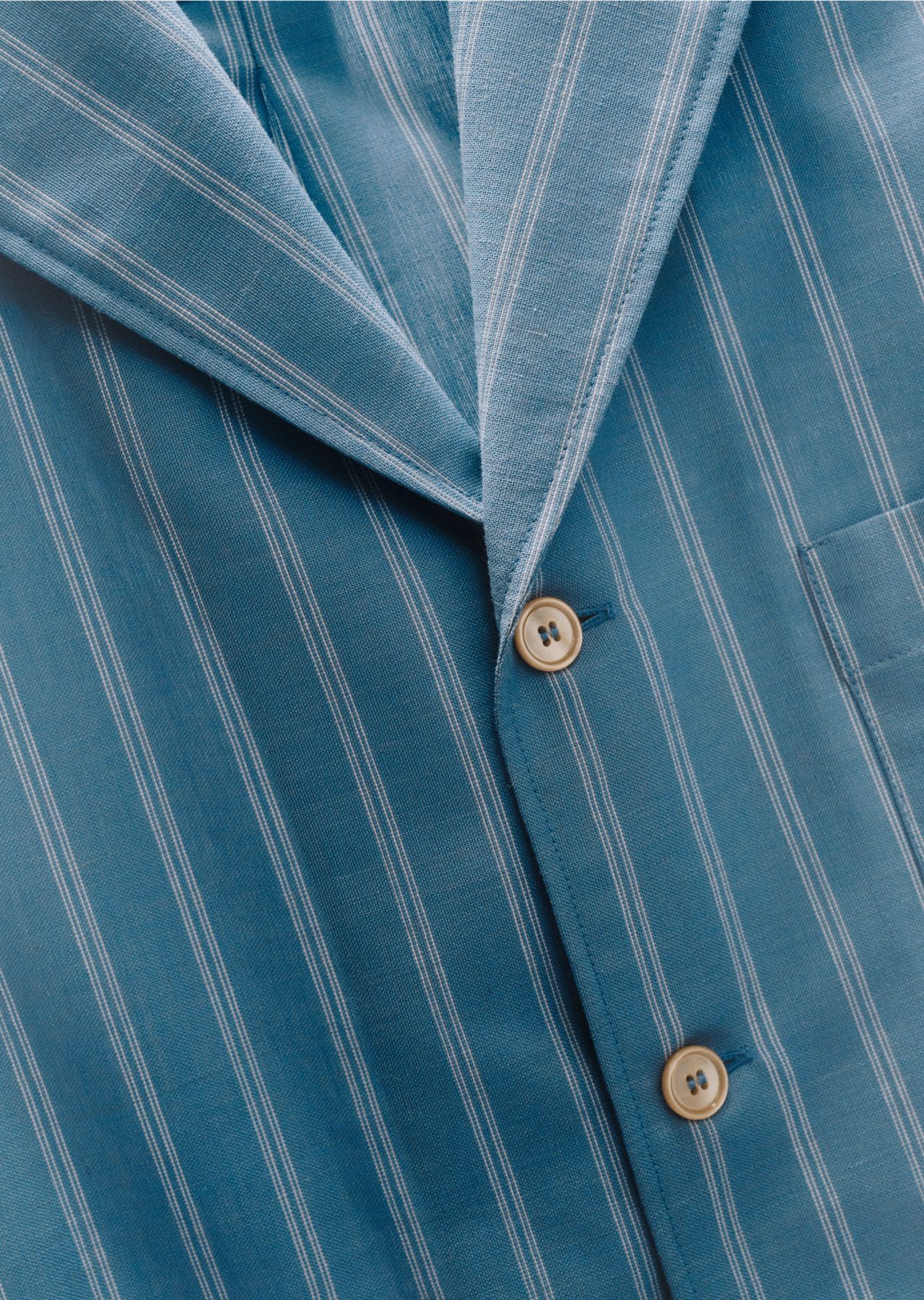 A blue pinstripe shirt with an open collar and tan buttons