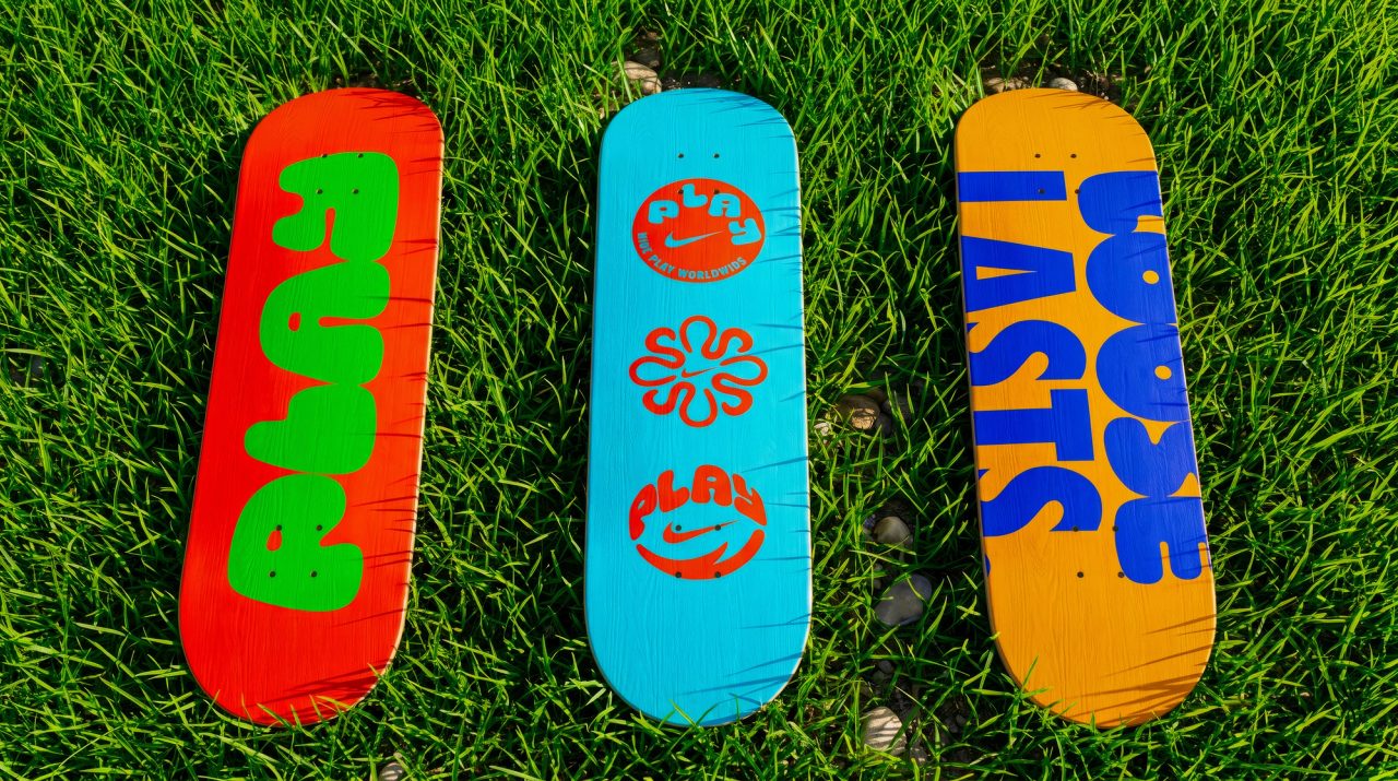 Three skateboard decks on grass in red, blue and orange, carrying PLAY and Loose Lasts graphics