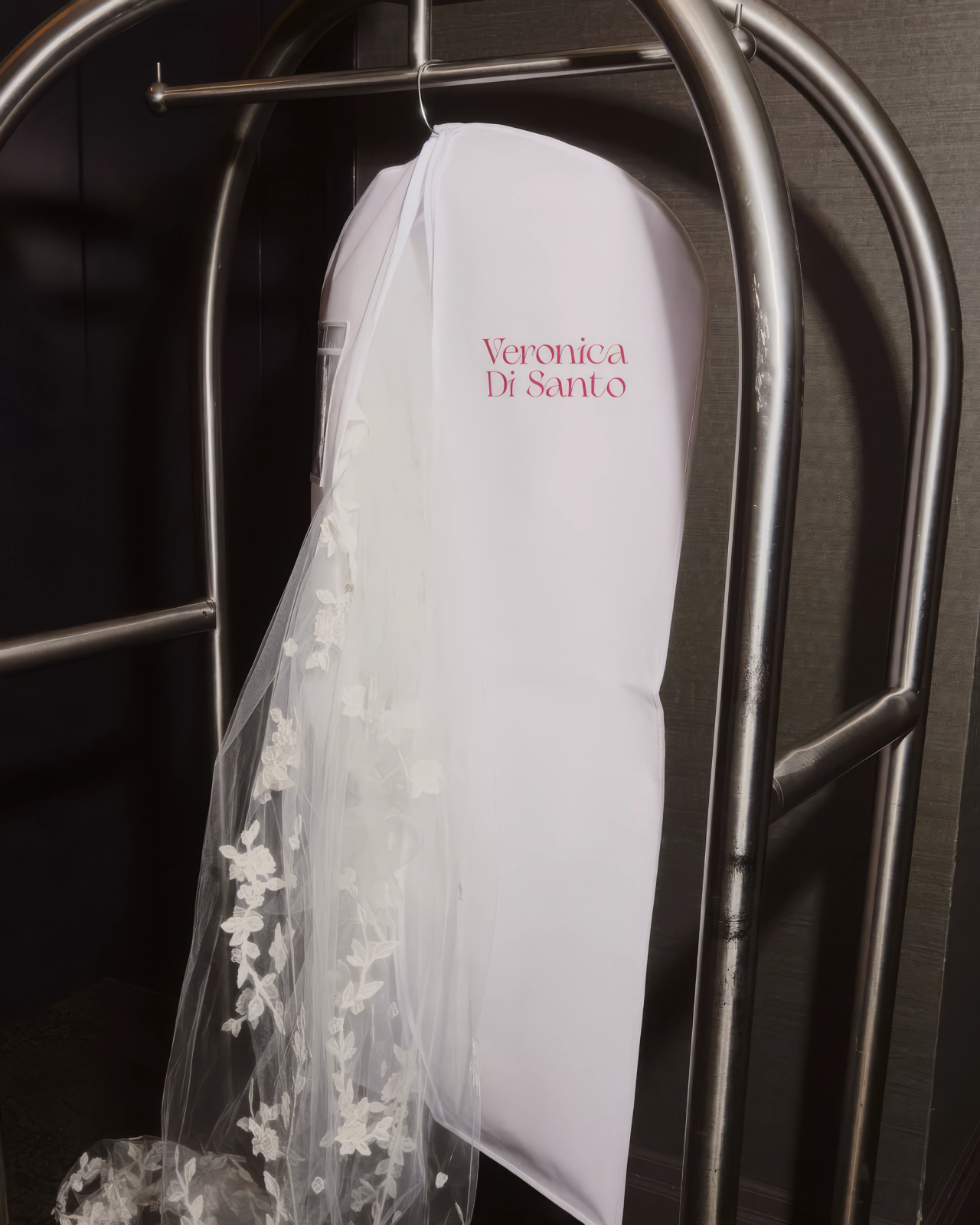 A Veronica Di Santo garment bag and floral lace veil on a luggage trolley