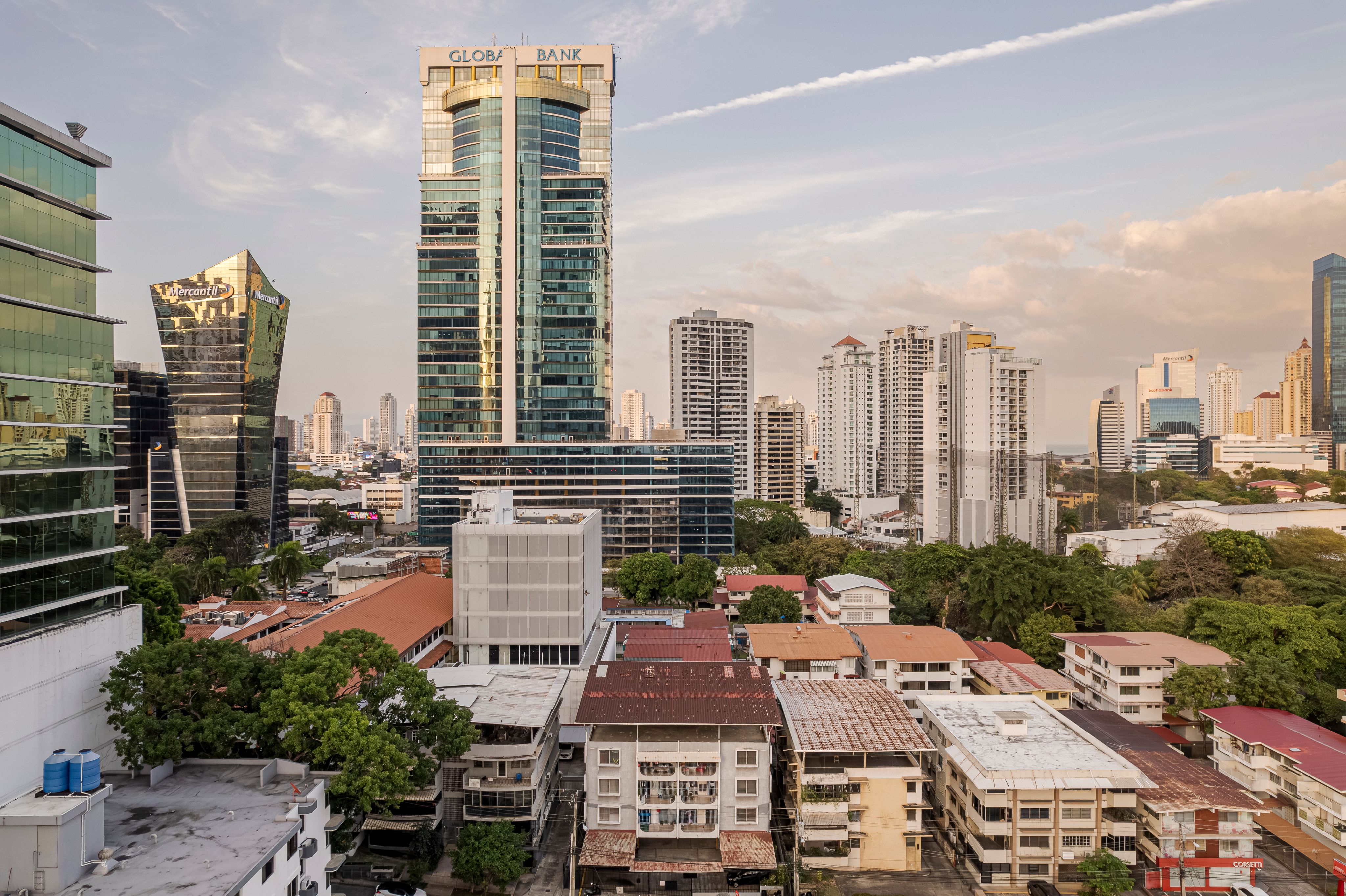 Vista aérea de una torre corporativa de cristal entre una densa mezcla de edificios de mediana altura y azoteas de la ciudad