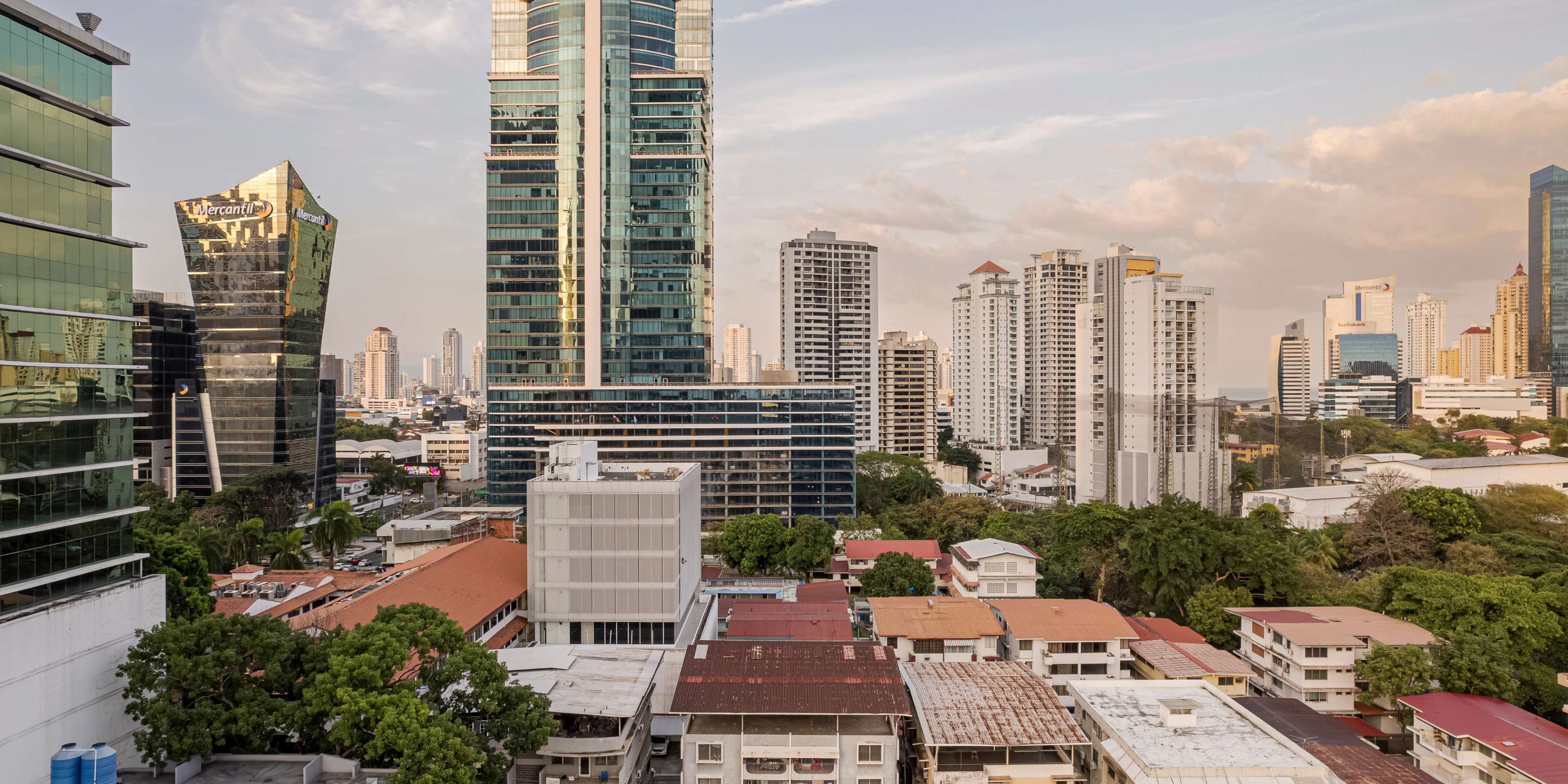 Vista aérea de una torre corporativa de cristal entre una densa mezcla de edificios de mediana altura y azoteas de la ciudad