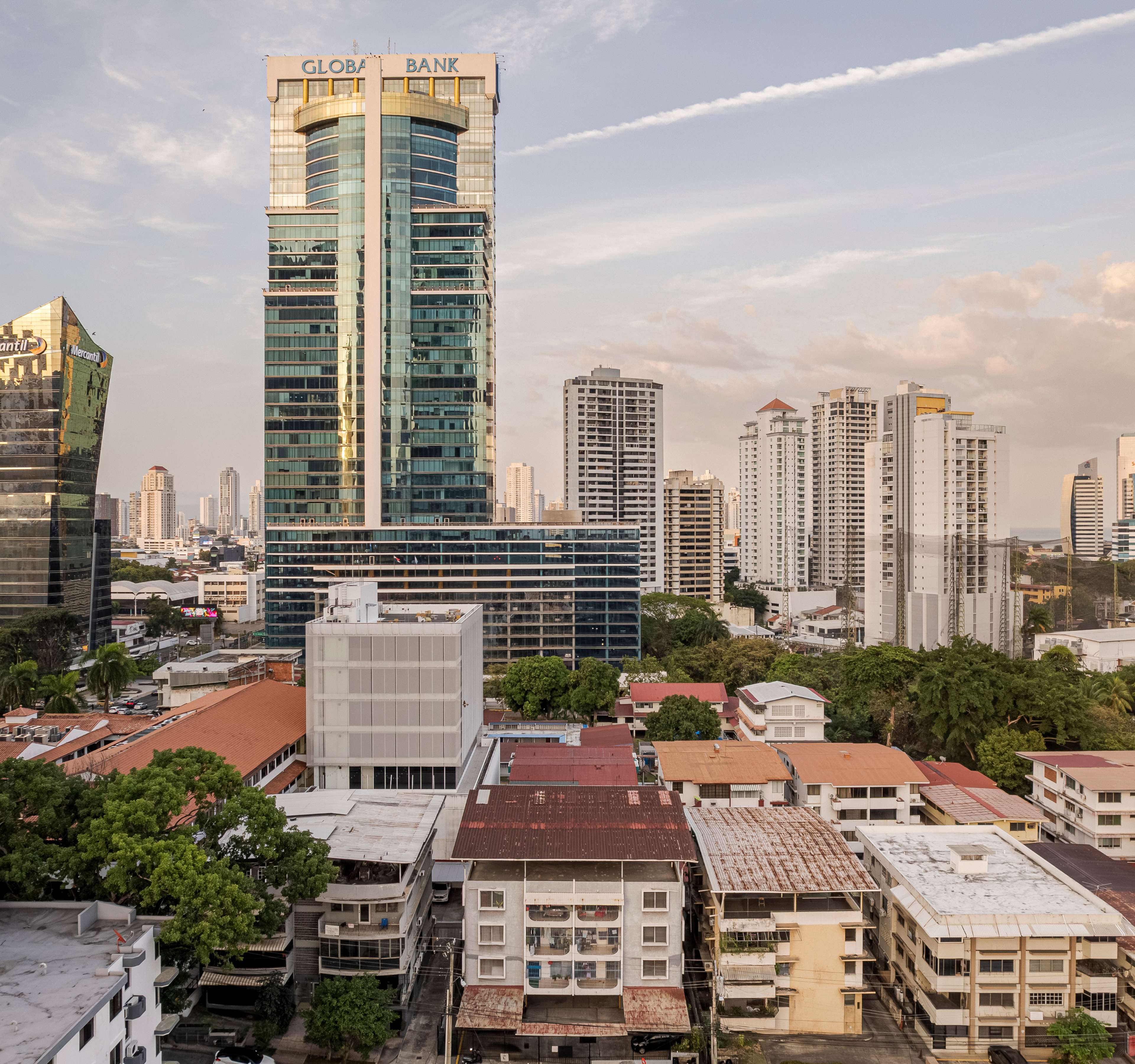 Vista aérea de una torre corporativa de cristal entre una densa mezcla de edificios de mediana altura y azoteas de la ciudad