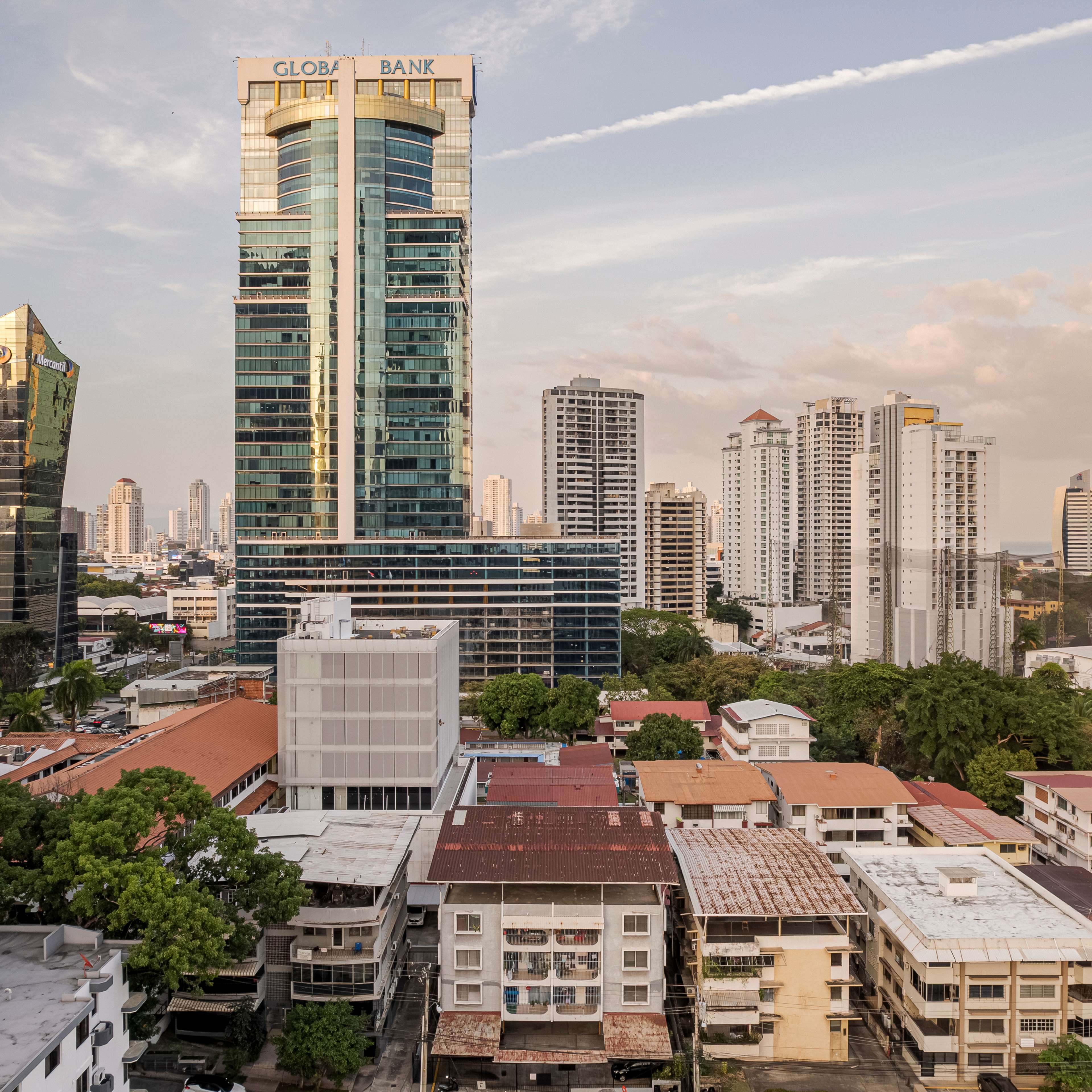 Vista aérea de una torre corporativa de cristal entre una densa mezcla de edificios de mediana altura y azoteas de la ciudad