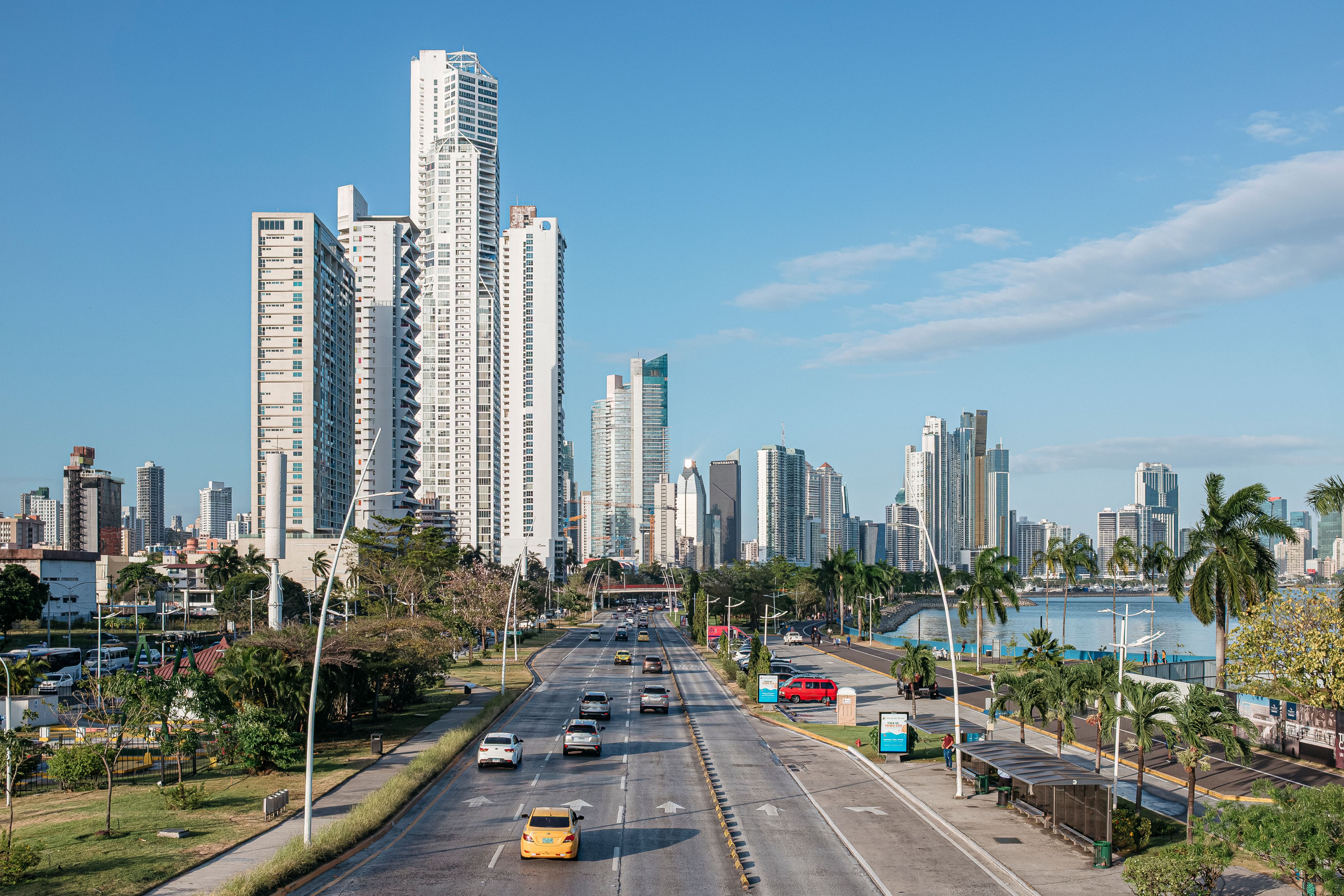El panorama urbano (skyline) de la Ciudad de Panamá con sus rascacielos a lo largo de una avenida costera, visto a través de una carretera de varios carriles bajo un cielo azul despejado