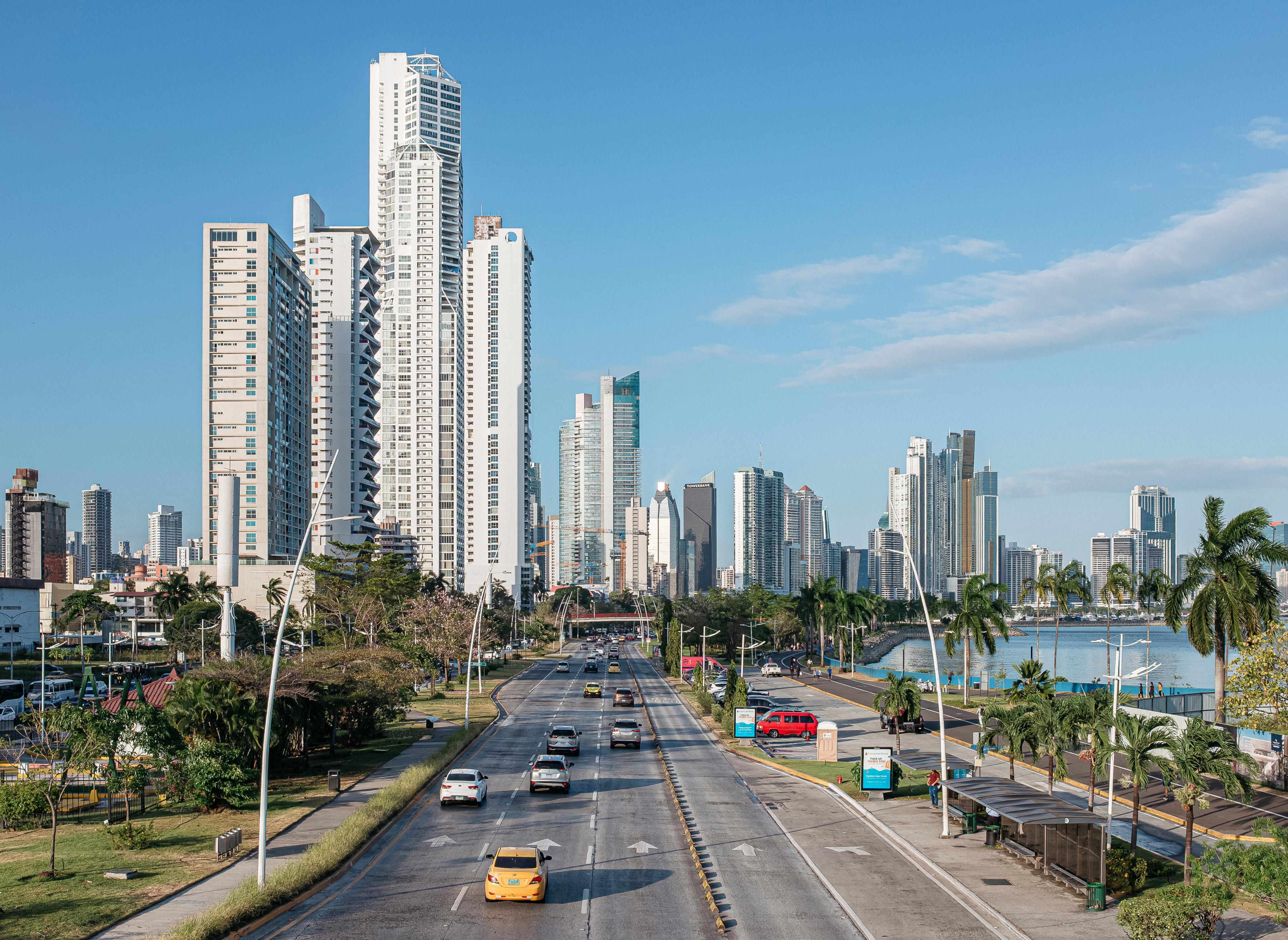 El panorama urbano (skyline) de la Ciudad de Panamá con sus rascacielos a lo largo de una avenida costera, visto a través de una carretera de varios carriles bajo un cielo azul despejado
