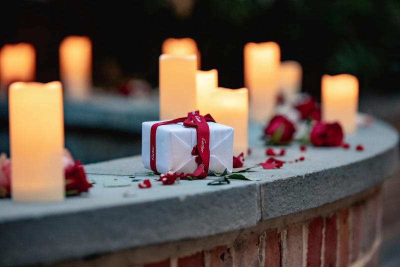 Romantic proposal setup in New Orleans with Cartier engagement ring box, candles, rose petals, and romantic decor.