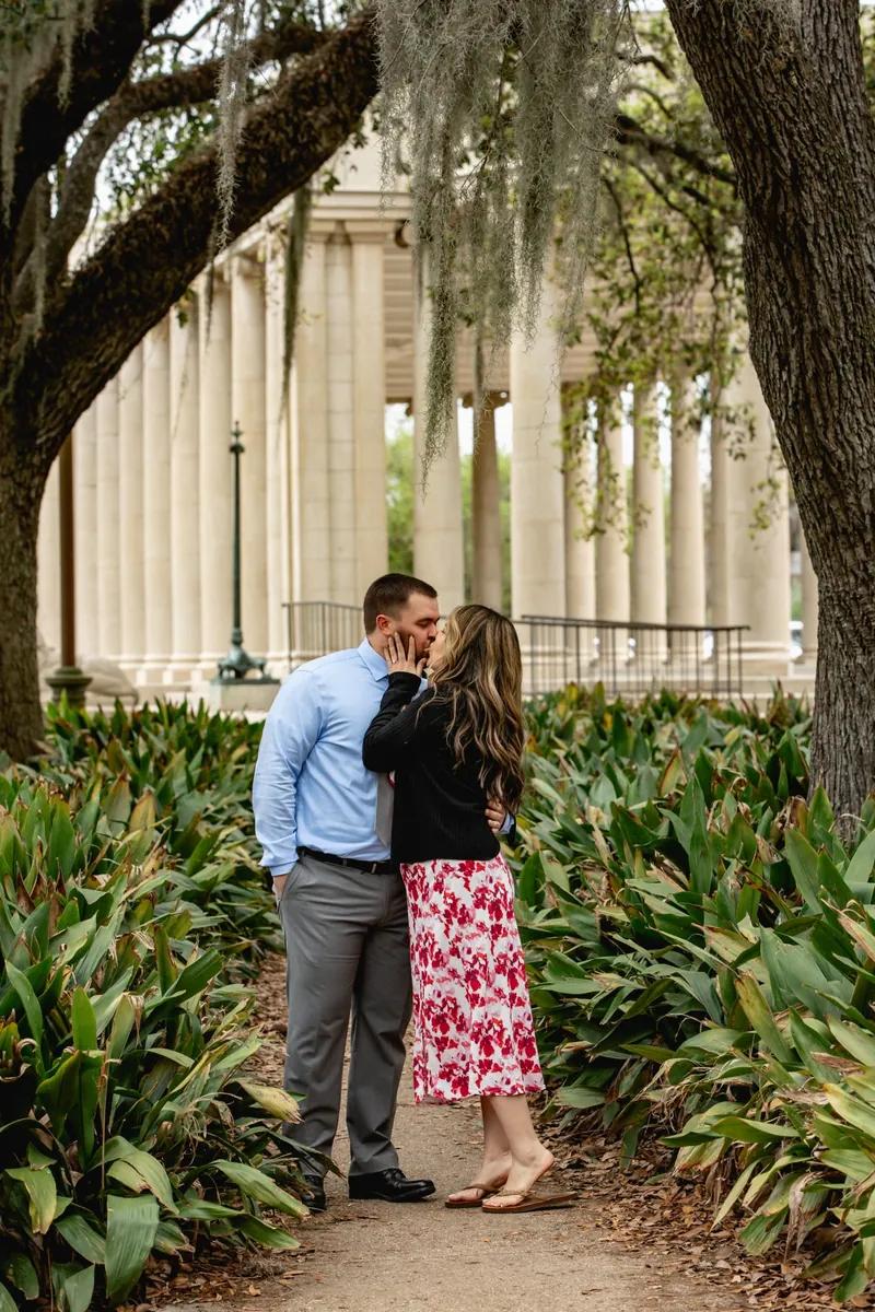 Romantic marriage proposal at City Park in New Orleans, couple kissing in front of columns after engagement.