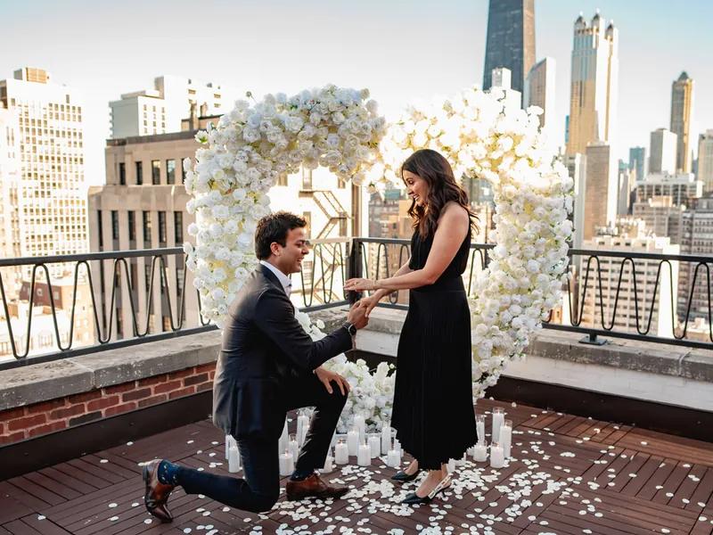 Private Chicago rooftop proposal with a white floral arch and rose petals