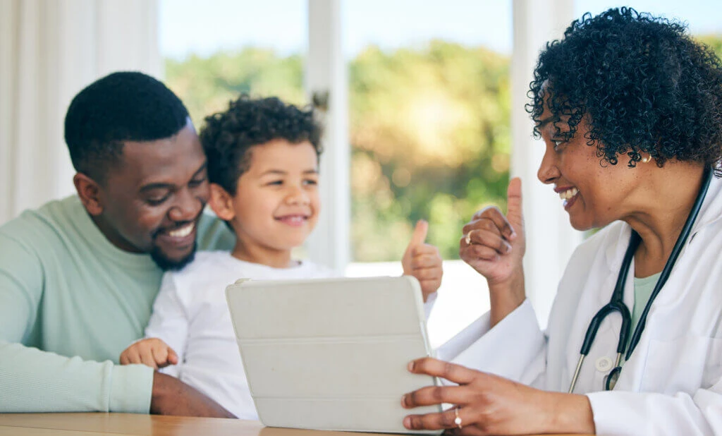 Pediatrician, father and child with thumbs up from patient edication on a tablet with good news. Happy kid, dad and doctor in a clinic consultation office with a healthcare worker and smile in hospital.