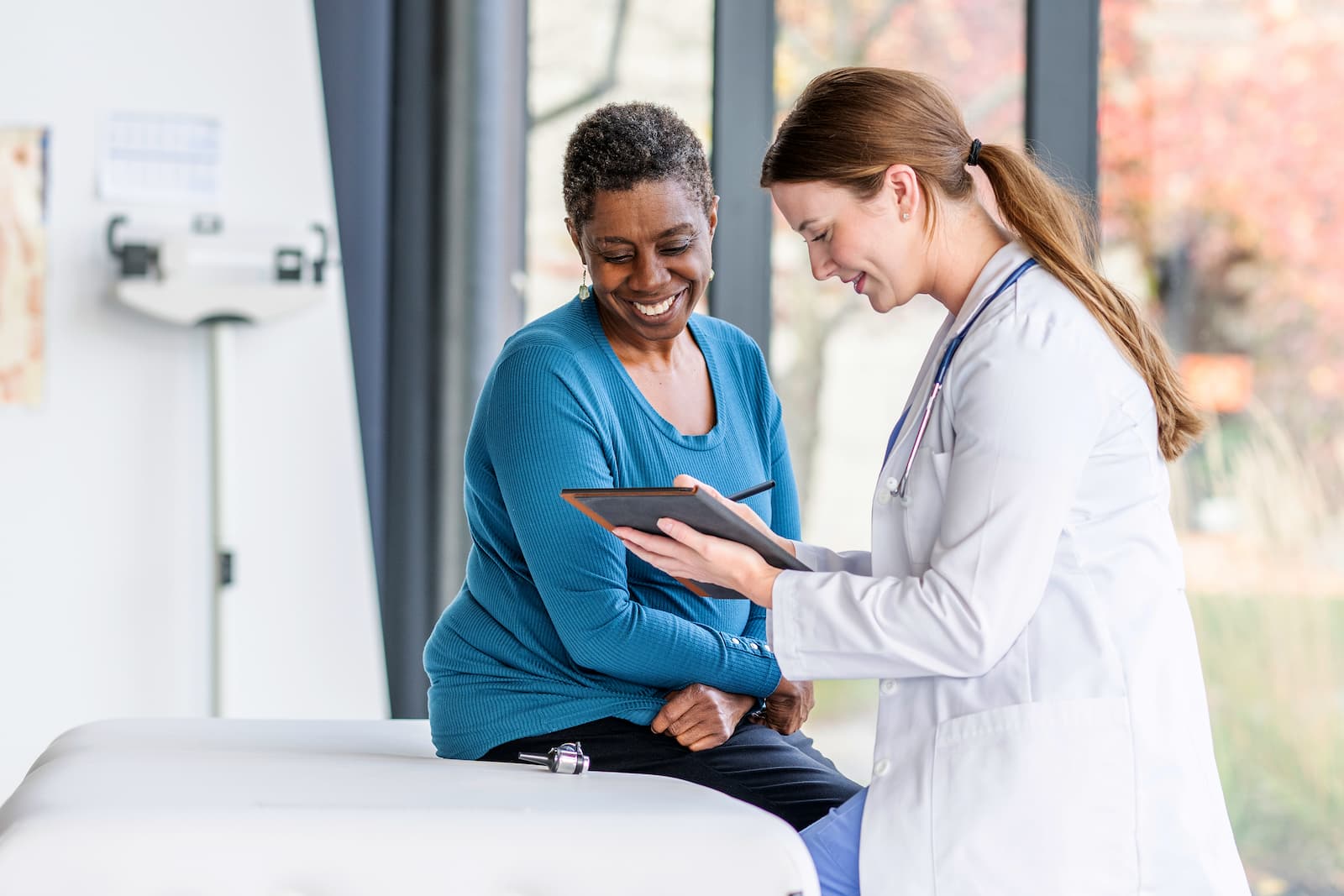 Doctor reviewing information on a tablet with a smiling patient in an exam room