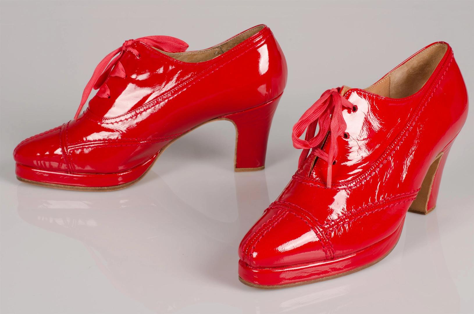 Rode glanzende herenschoenen met hoge hakken.