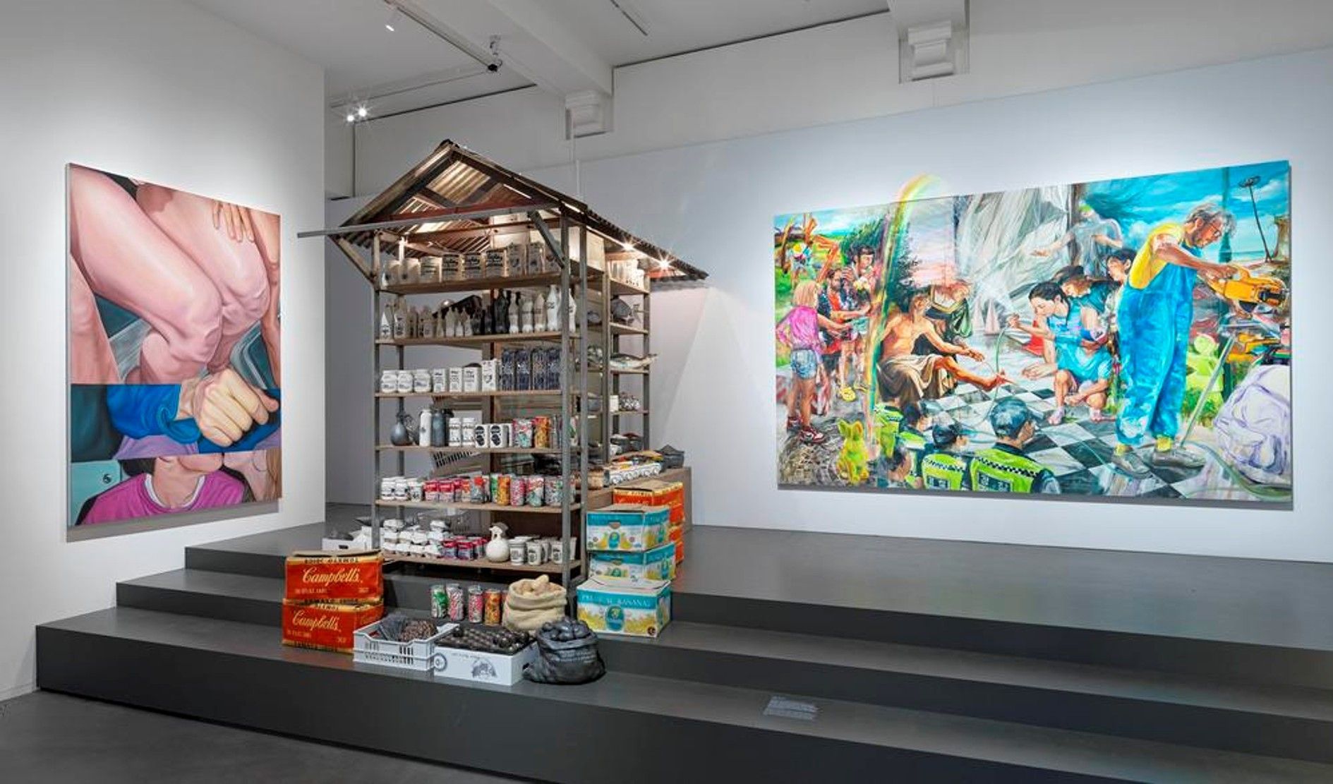 Een museumzaal met een marktkraam met replica's van groente, fruit en consumentenproducten, met opschriften, in bakken en kratten.