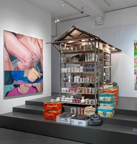 Een museumzaal met een marktkraam met replica's van groente, fruit en consumentenproducten, met opschriften, in bakken en kratten.