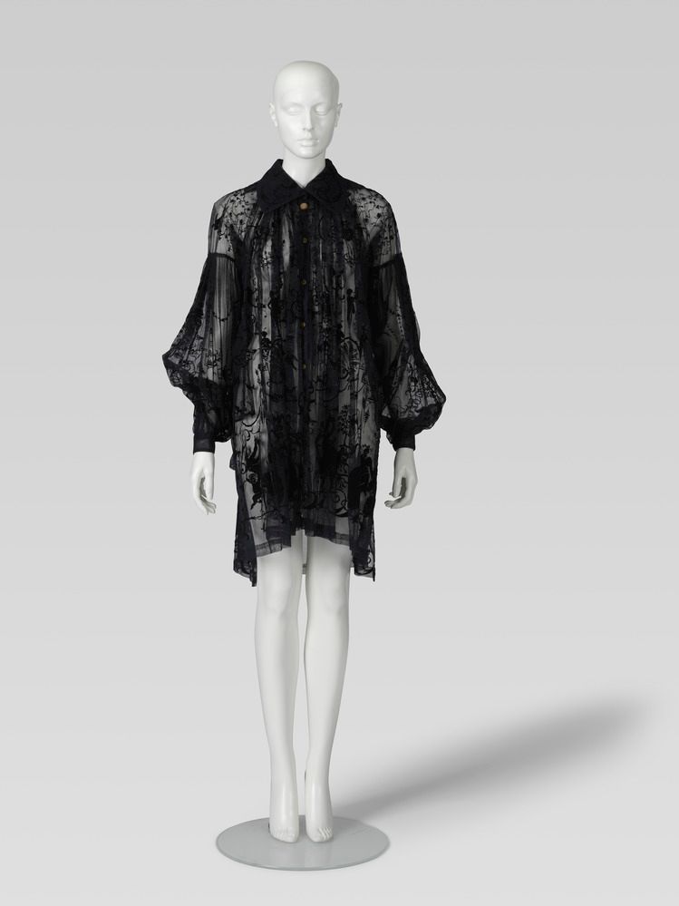 Sheer black blouse dress by fashion designer Vivienne Westwood, featuring a delicate embroidered pattern, collar and voluminous sleeves, displayed on a mannequin. 