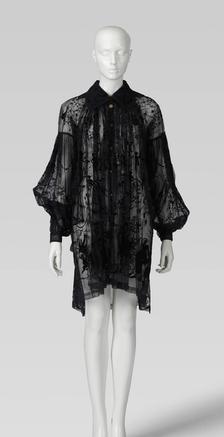 Sheer black blouse dress by fashion designer Vivienne Westwood, featuring a delicate embroidered pattern, collar and voluminous sleeves, displayed on a mannequin.