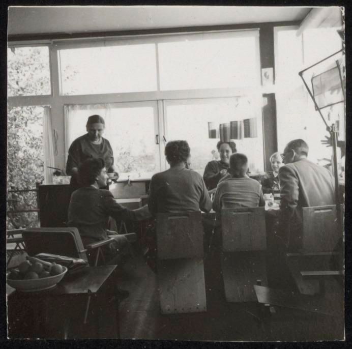 Zwart-witfoto van groep mensen zittend aan tafel in het Rietveld Schröderhuis.