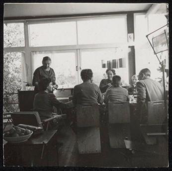 Zwart-witfoto van groep mensen zittend aan tafel in het Rietveld Schröderhuis.