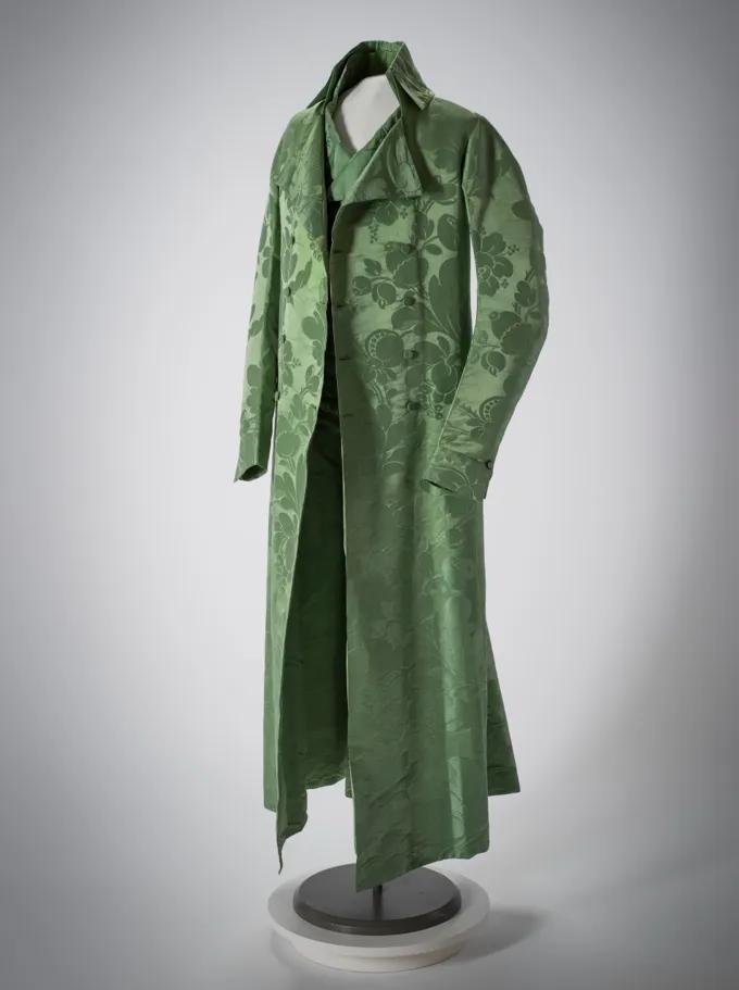 De nauwsluitende groene jas met ingenaaid vest met patroon van bloemen, bladeren en granaatappels