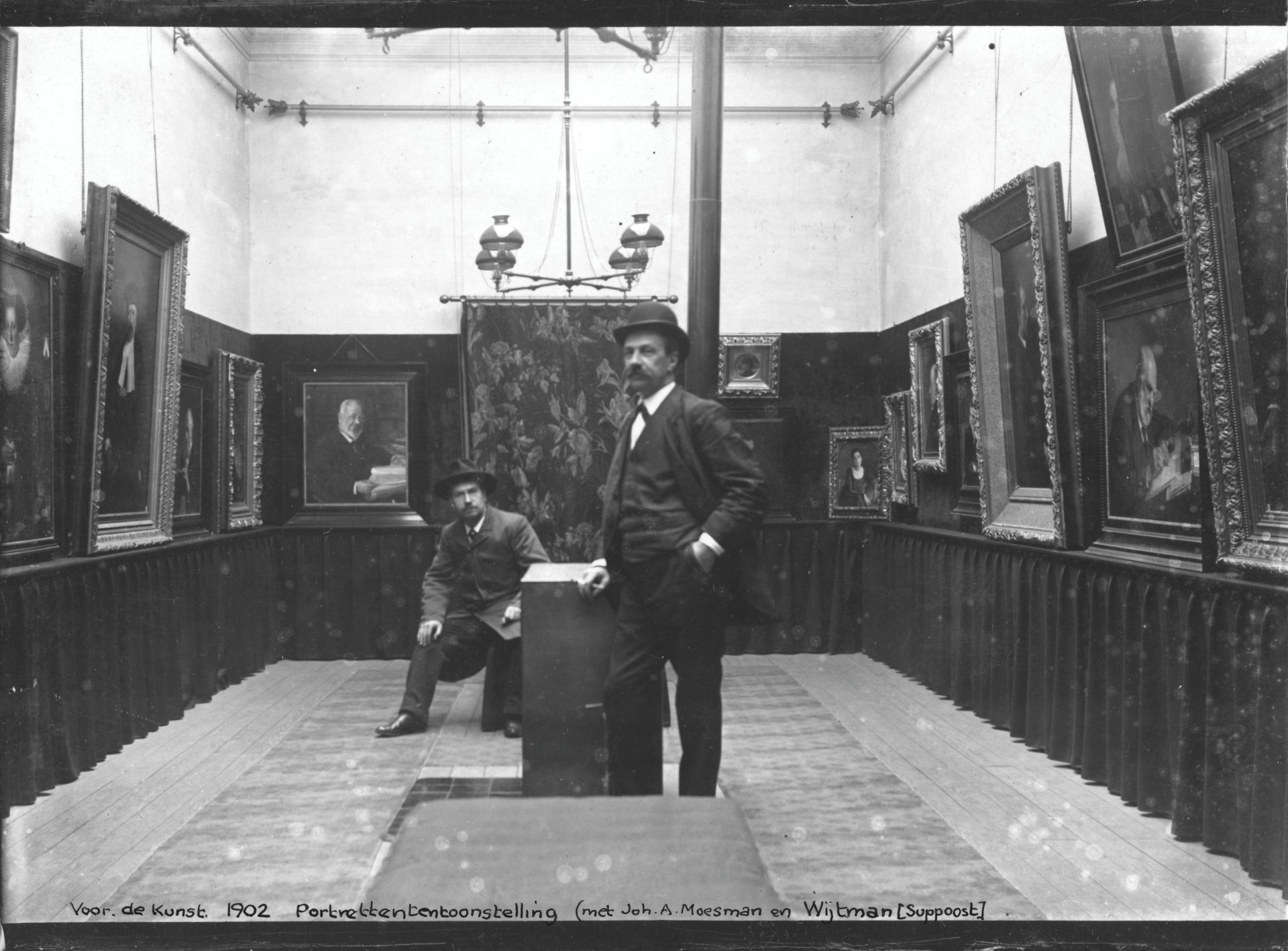 Twee mannen staan ​​in een museumzaal met hangende kunstwerken.