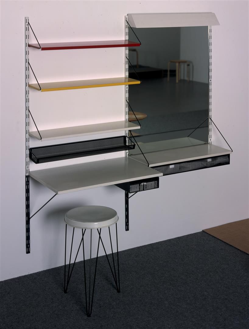 Kaptafel van gekleurde metalen plankjes, rechts een grote spiegel met lade eronder, en een metalen krukje