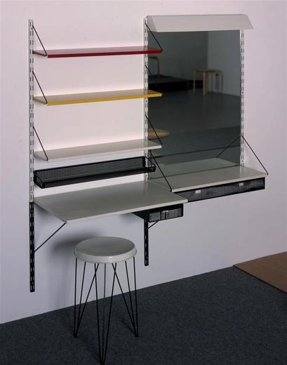 Kaptafel van gekleurde metalen plankjes, rechts een grote spiegel met lade eronder, en een metalen krukje