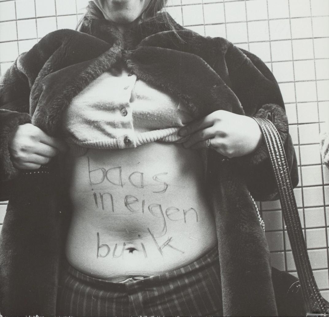 Vrouw houdt haar kleding omhoog met twee handen, op haar buik staat geschreven 'baas in eigen buik'.