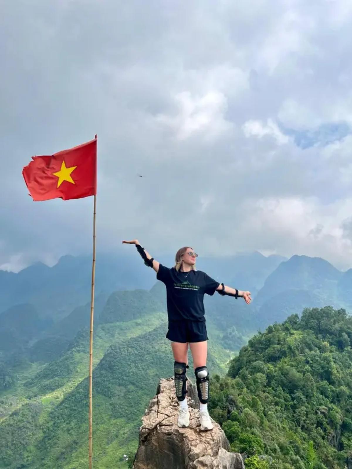A traveler standing on a peak beside a Vietnamese flag in Ha Giang