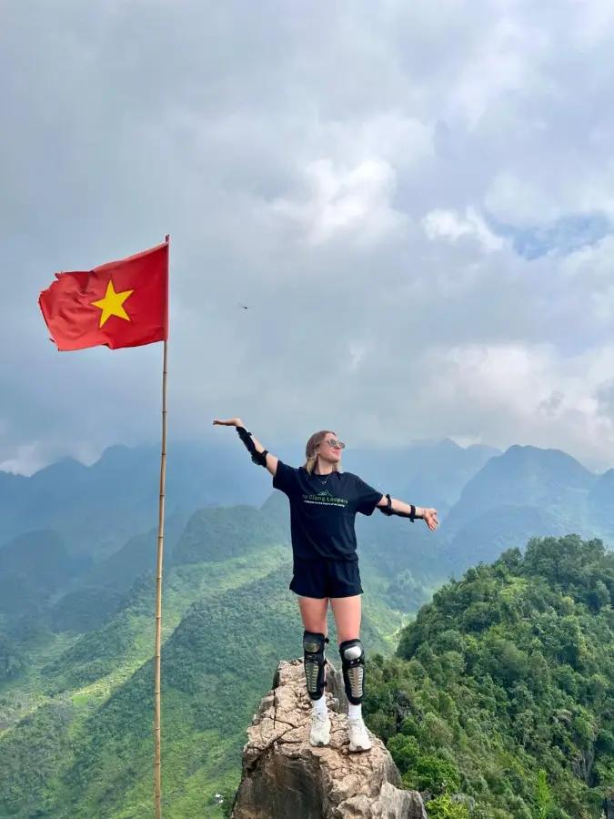 A traveler standing on a peak beside a Vietnamese flag in Ha Giang