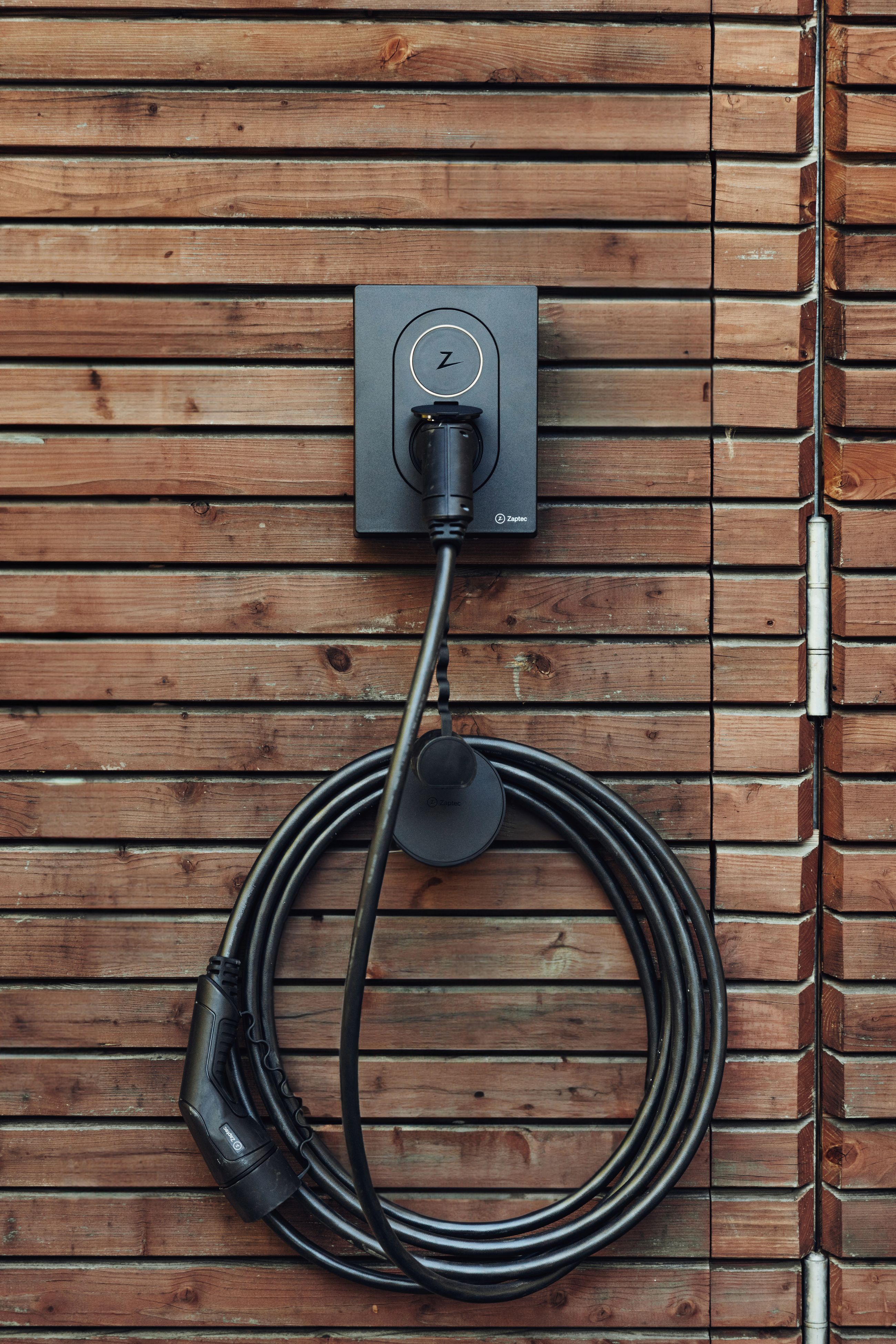 Elbillader av typen Zaptec Go montert på yttervegg med ladekabel pent opphengt – for trygg og praktisk lading hjemme.