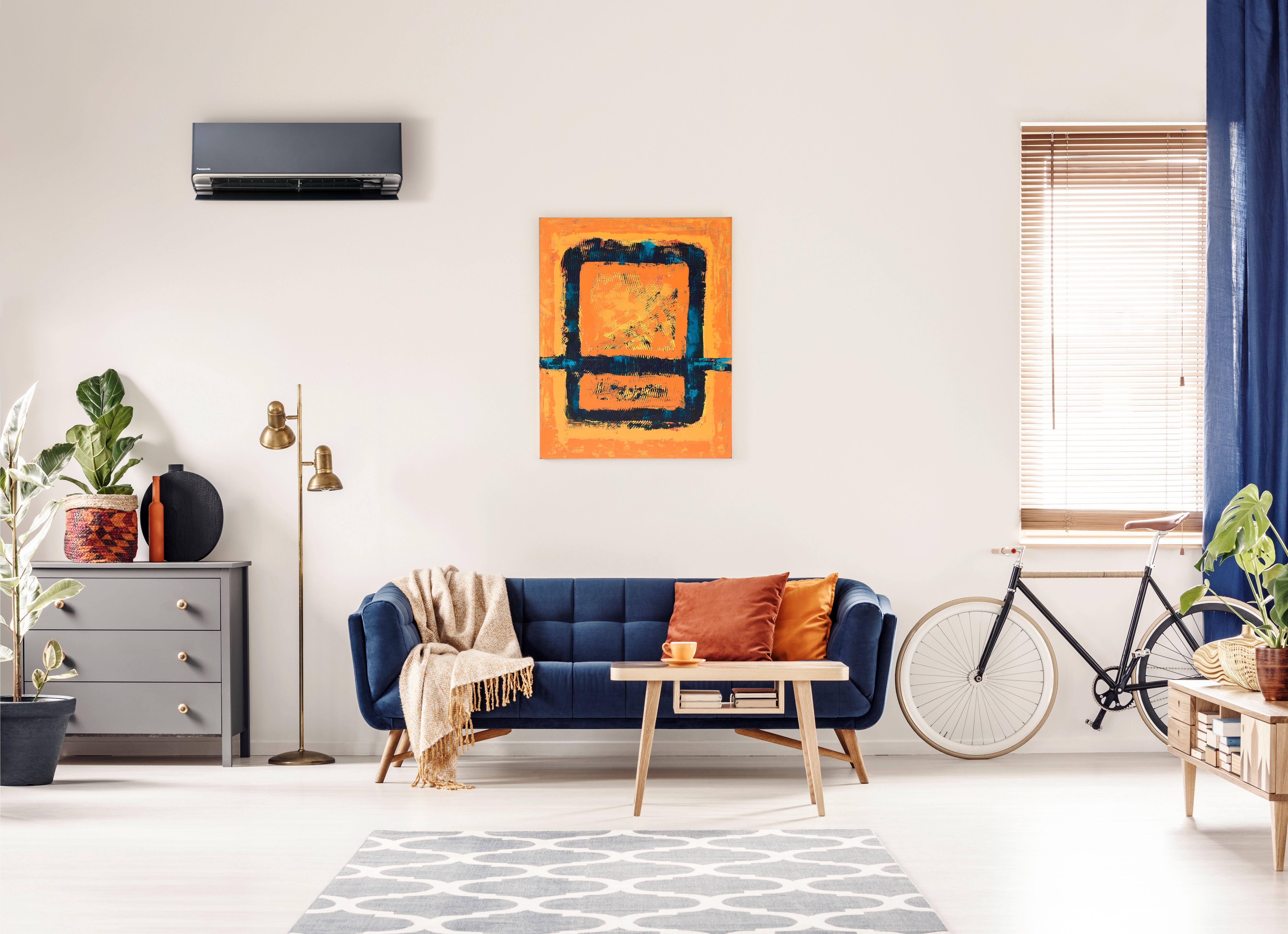 Sort Panasonic Flagship 7.5 fra Ishavskraft montert i moderne og fargerik stue med blå sofa, kunst på veggen og grønne planter – montering og nedbetaling over strømregningen inkludert