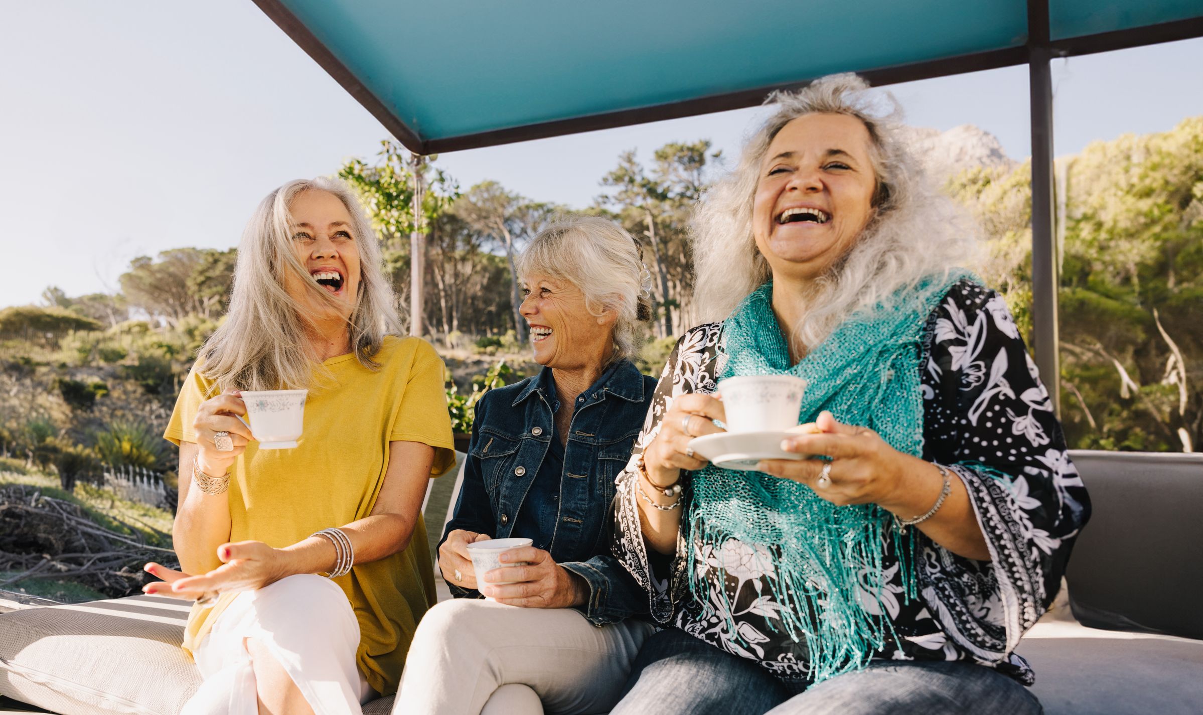 Tre damer i sin beste alder drikker kaffe i sola og morer seg.