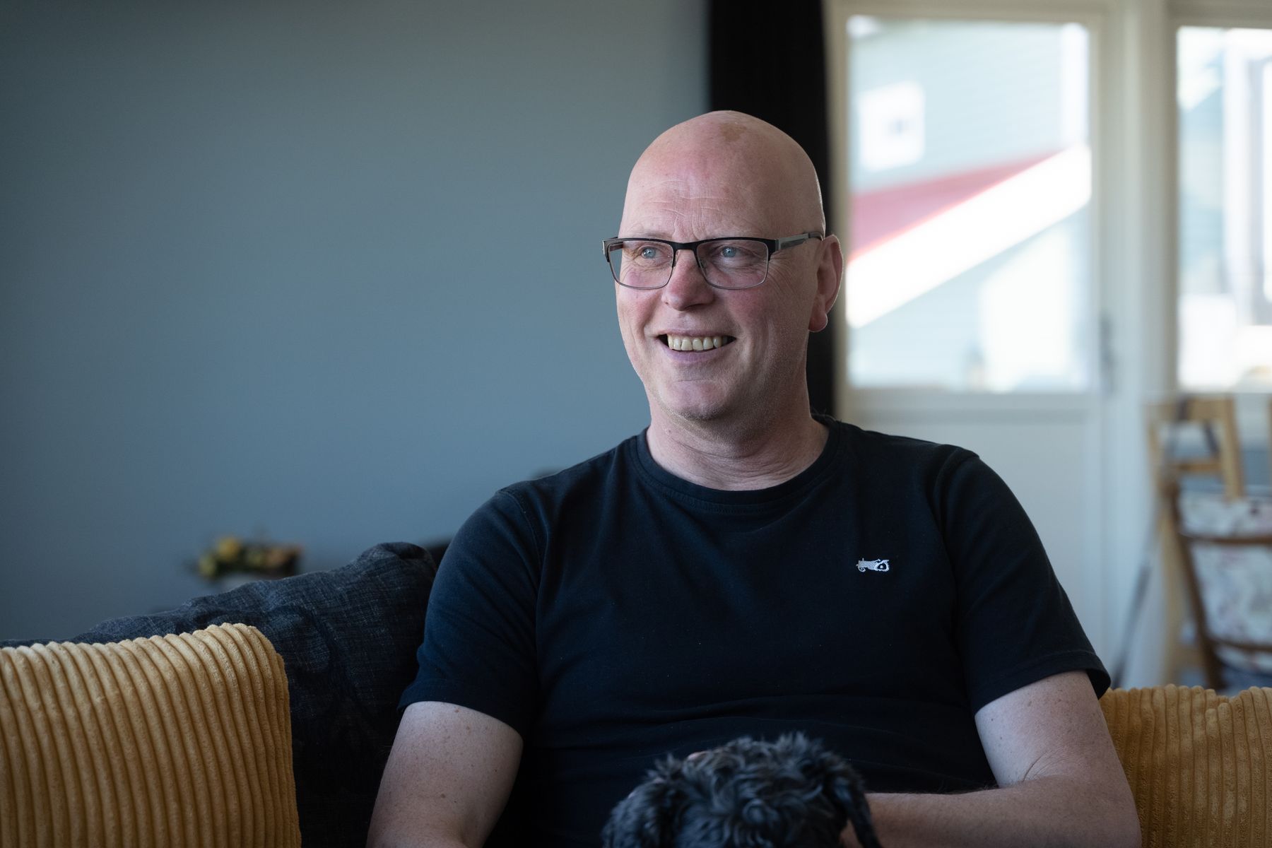 Alf Kondrad sitter i en sofa og smiler