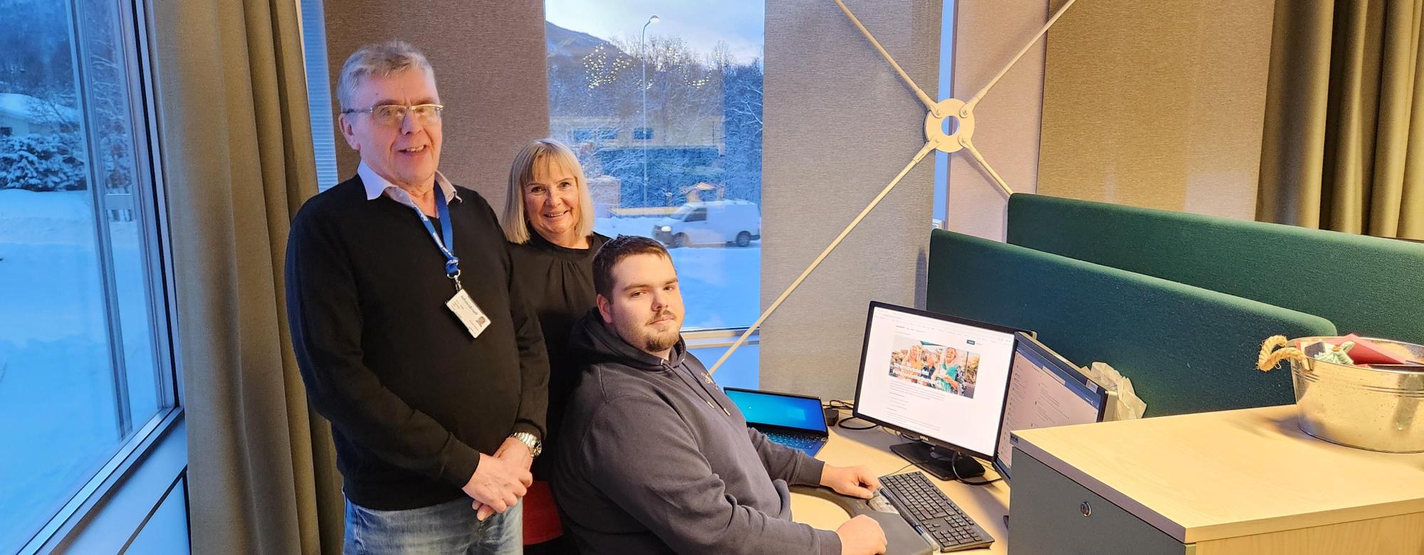 Idar, Gunn Tove og Magnus står stolte og smilende ved siden av kontorpulten hvor nettsiden for seniorstrøm med Ishavskraft lyser fra PC-skjermen