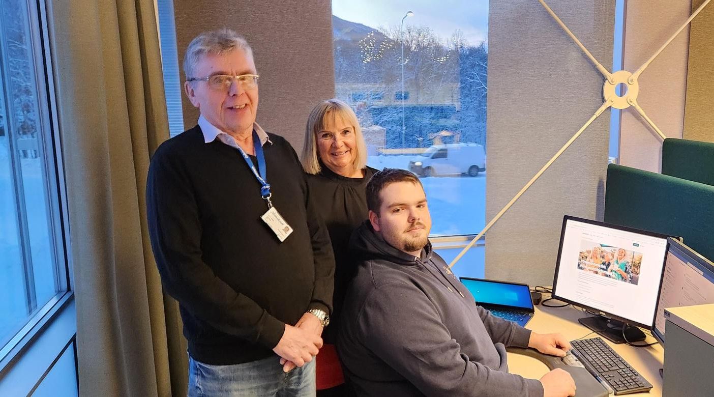 Idar, Gunn Tove og Magnus står stolte og smilende ved siden av kontorpulten hvor nettsiden for seniorstrøm med Ishavskraft lyser fra PC-skjermen