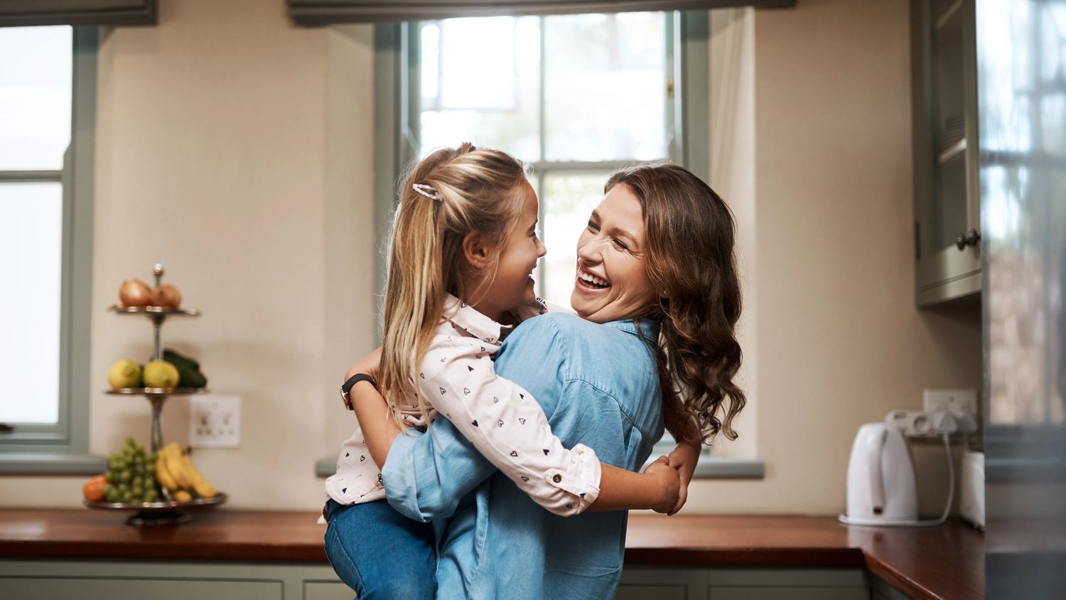 Smilende mor holder datteren sin på kjøkkenet – symbol på trygghet, komfort og forutsigbarhet med BoSpot strømavtale fra Ishavskraft.