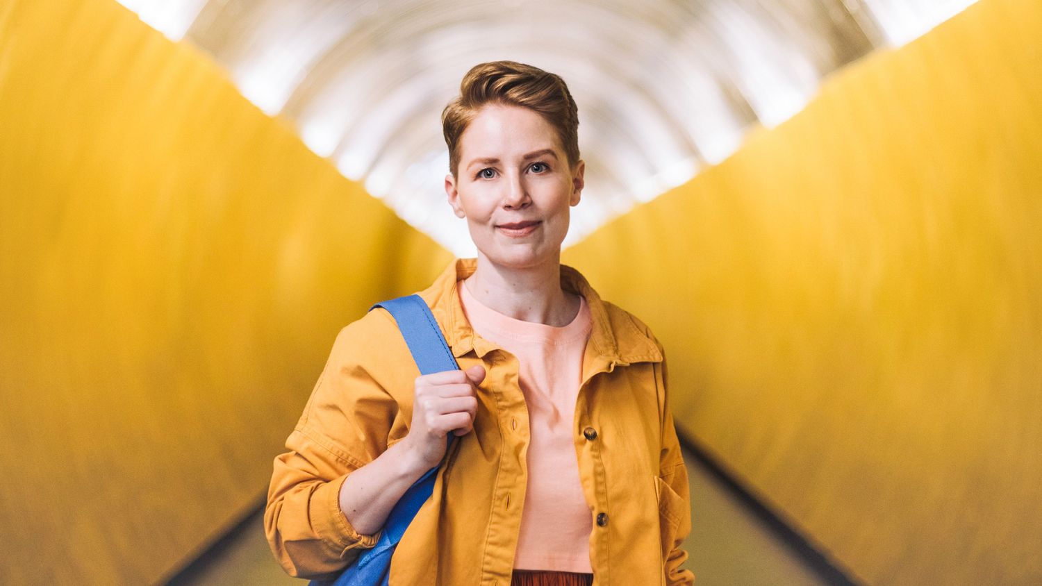 Person med gul jakke og blå veske i en moderne, gul tunnel – symbol på trygghet og fremtidsrettet energi fra Ishavskraft