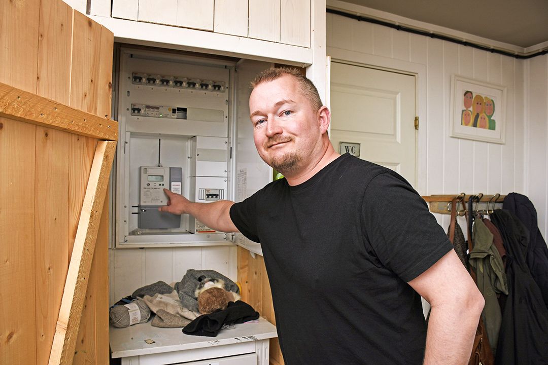 En mann i svart t-skjorte peker inn i et åpent sikringsskap, og illustrerer viktigheten av å jevne ut strømforbruket.