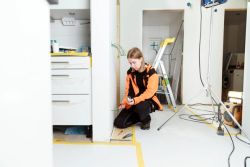 Elektriker bruker skrutrekker for å montere lys eller elektrisk utstyr under renovering av bad eller vaskerom.