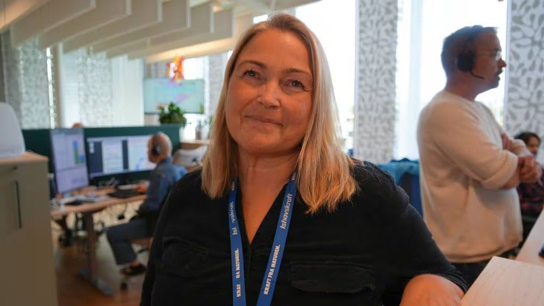 Elin Eriksen, leder for kundeservice, Ishavskraft, står i lokalene til selskapet og smiler. I bakgrunnen kan man se kundeservice på telefonene.