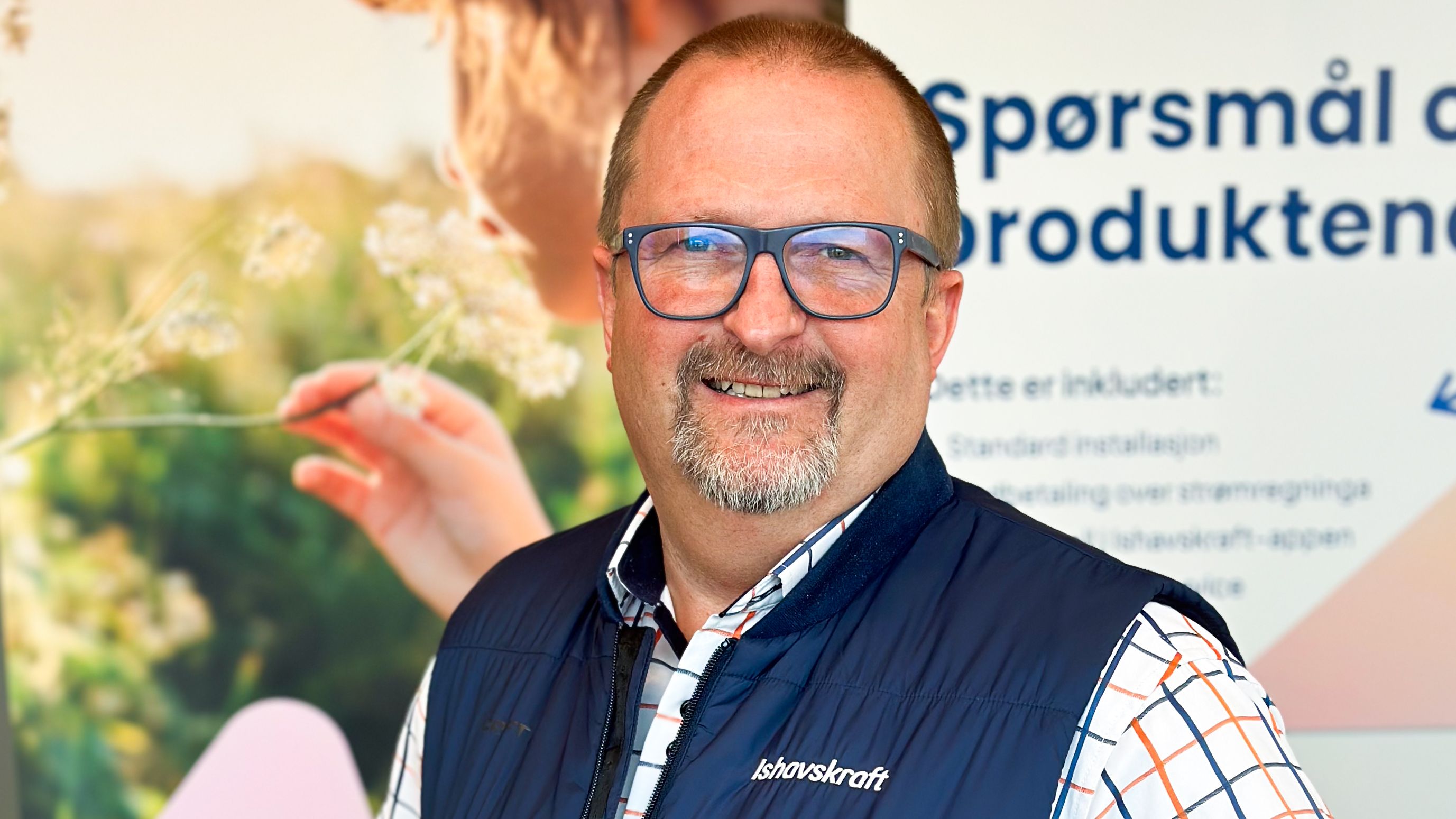 Stig A. Hanssen står foran plakater i lokalene til Ishavskraft og smiler til kameraet