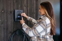 Kvinne som plugger inn en Zaptec Go elbillader på husvegg – trygg og brukervennlig lading hjemme.