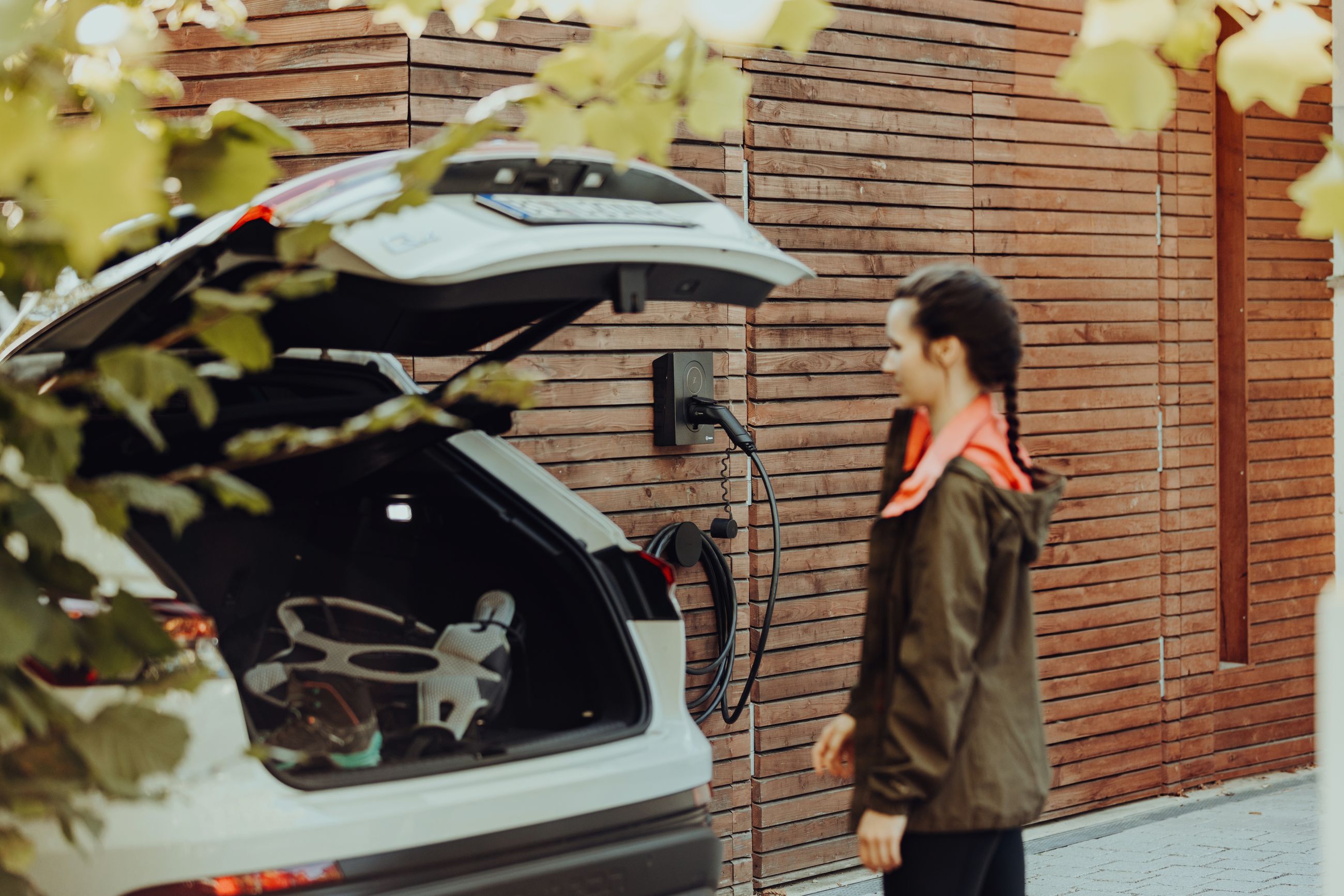 Kvinne ved elbil under lading med Zaptec Go hjemme – trygg og smart hjemmelading med ladekabel montert på yttervegg.