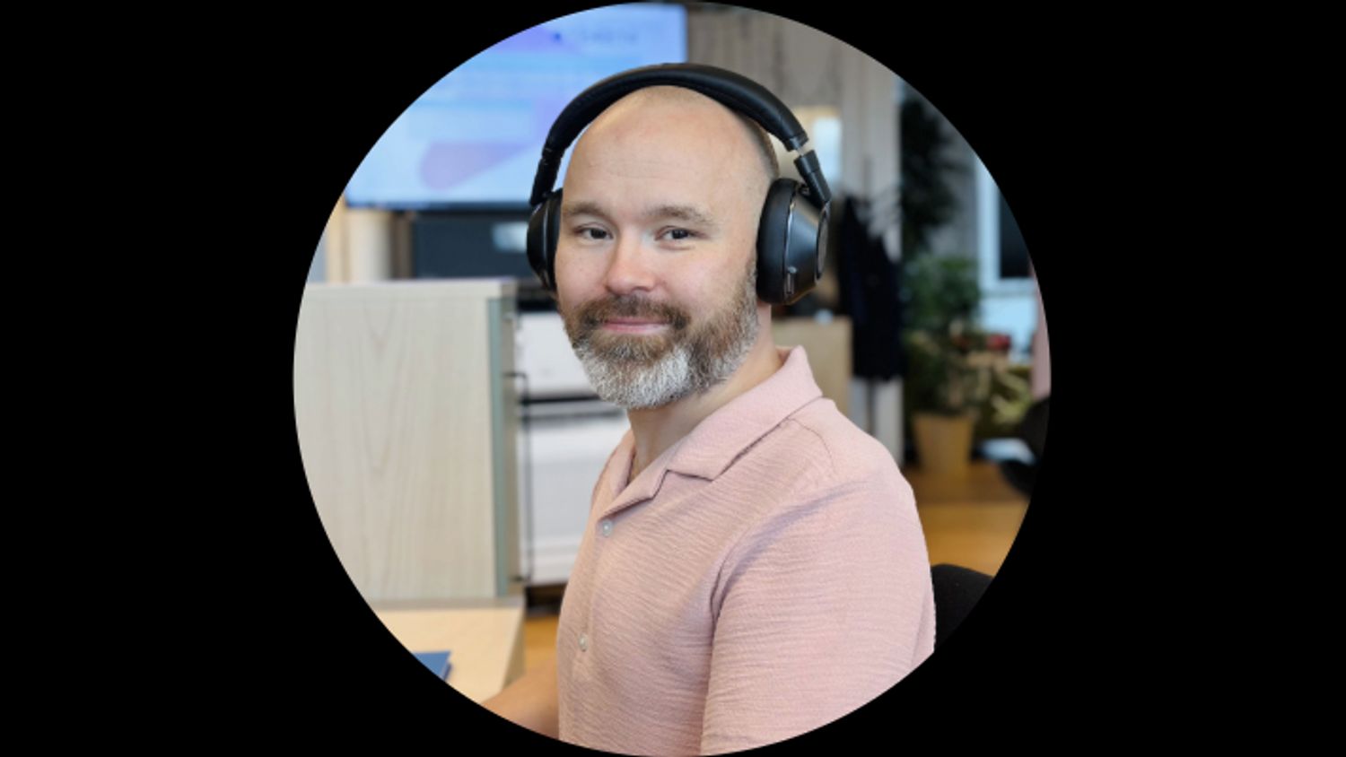 Smilende kunderådgiver med hodetelefoner og rosa skjorte sitter på kontoret